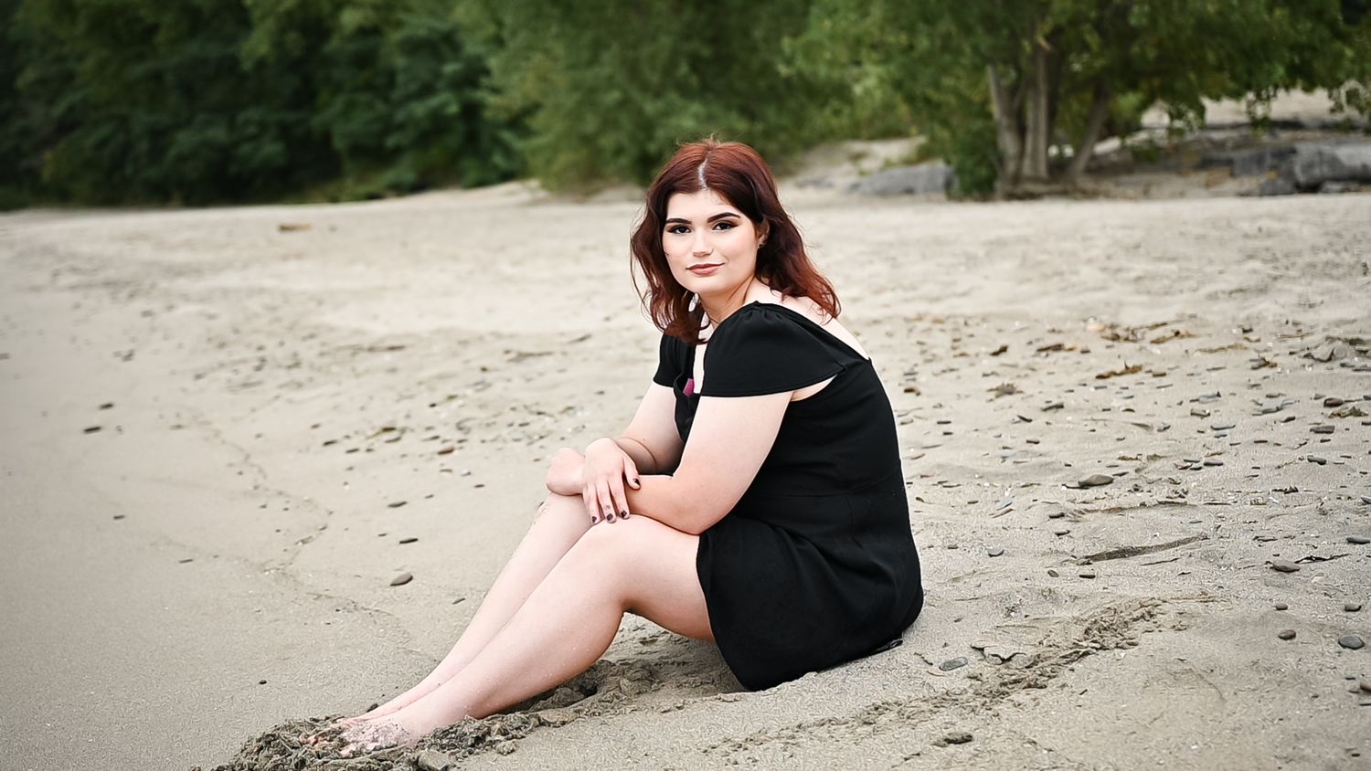 Seated pose on a sandy beach wearing a black dress.