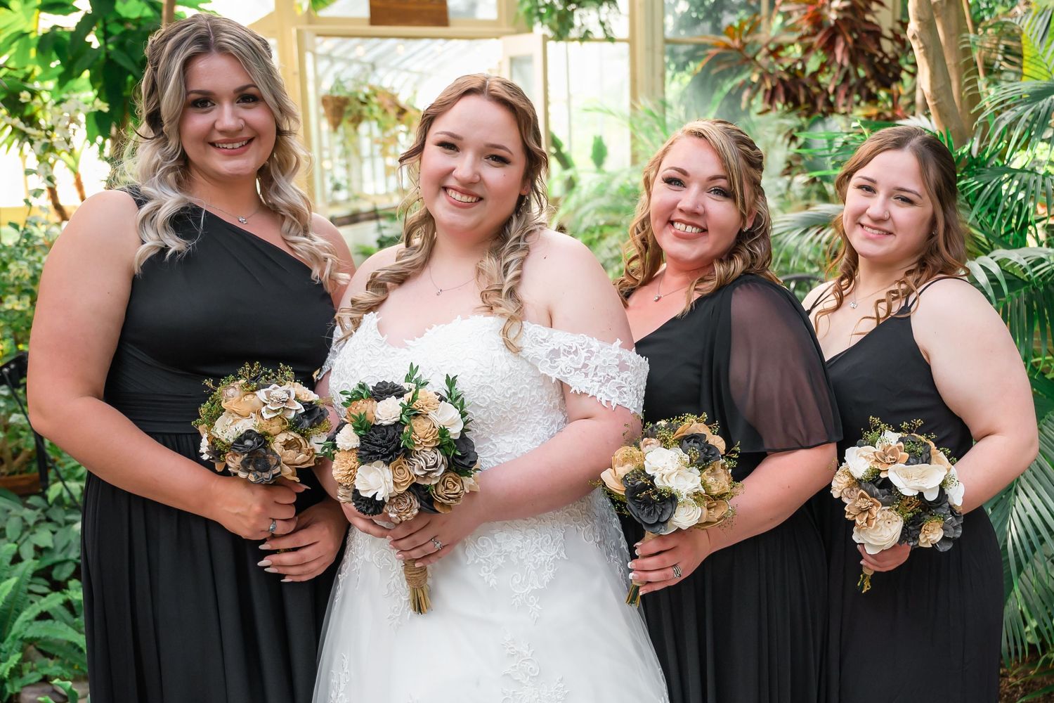 A bridal party poses with matching bouquets featuring black bridesmaid dresses in a tropical garden setting.