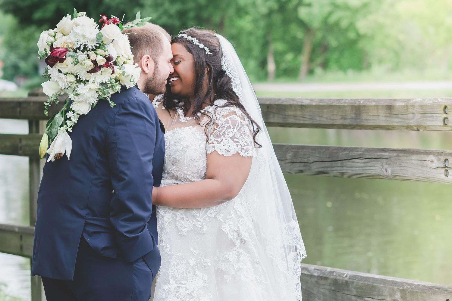 A sweet wedding moment captured near a rustic wooden fence with white floral bouquet.