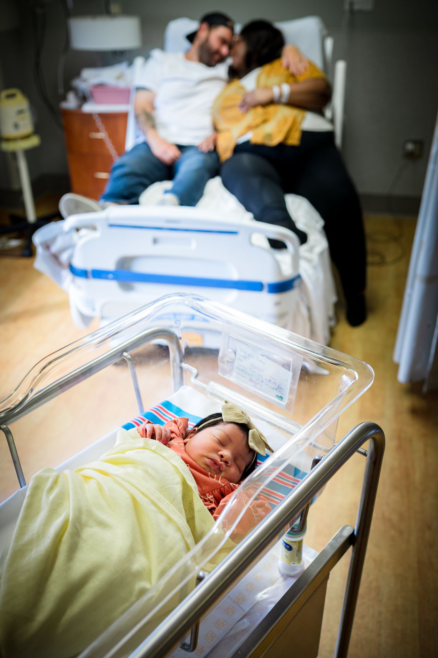 Medical staff tend to a newborn baby resting in a hospital bassinet under monitoring equipment.