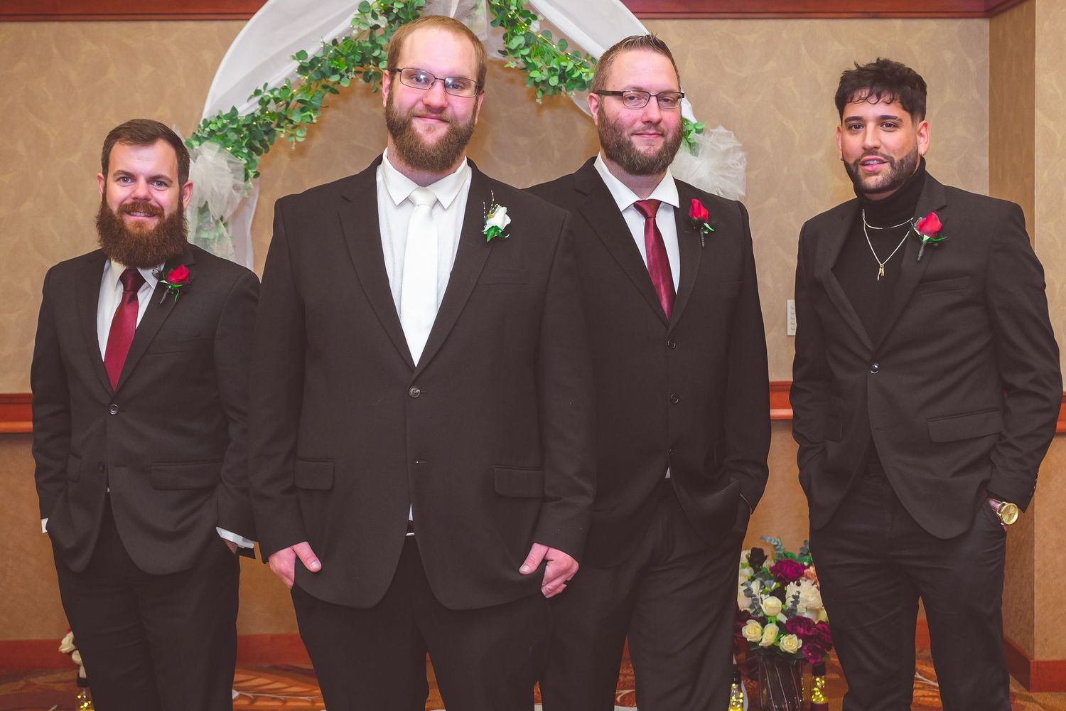 Four groomsmen in formal attire pose together during a wedding ceremony.