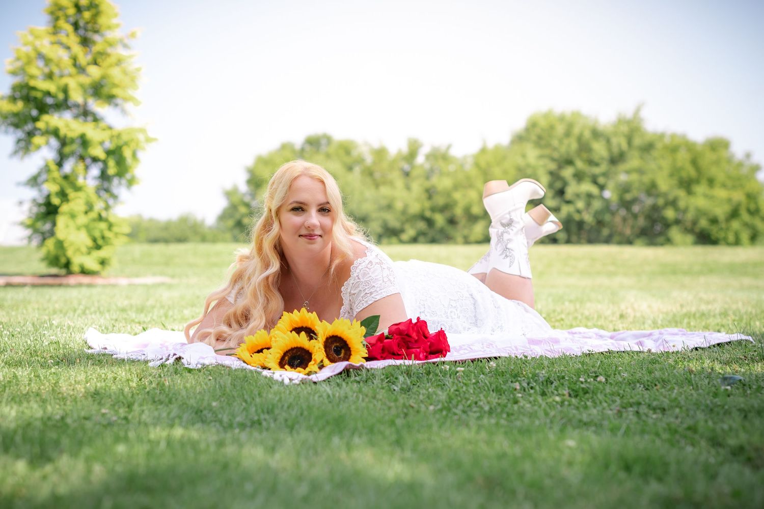 A relaxed outdoor photo shoot with sunflowers and roses on a white blanket.
