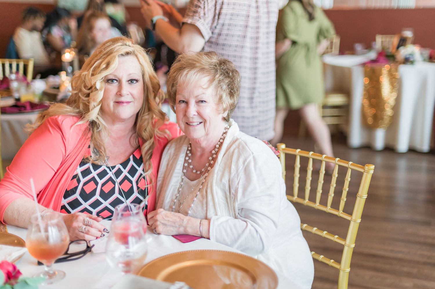 Two women in bright attire sharing a laugh at formal dining table.