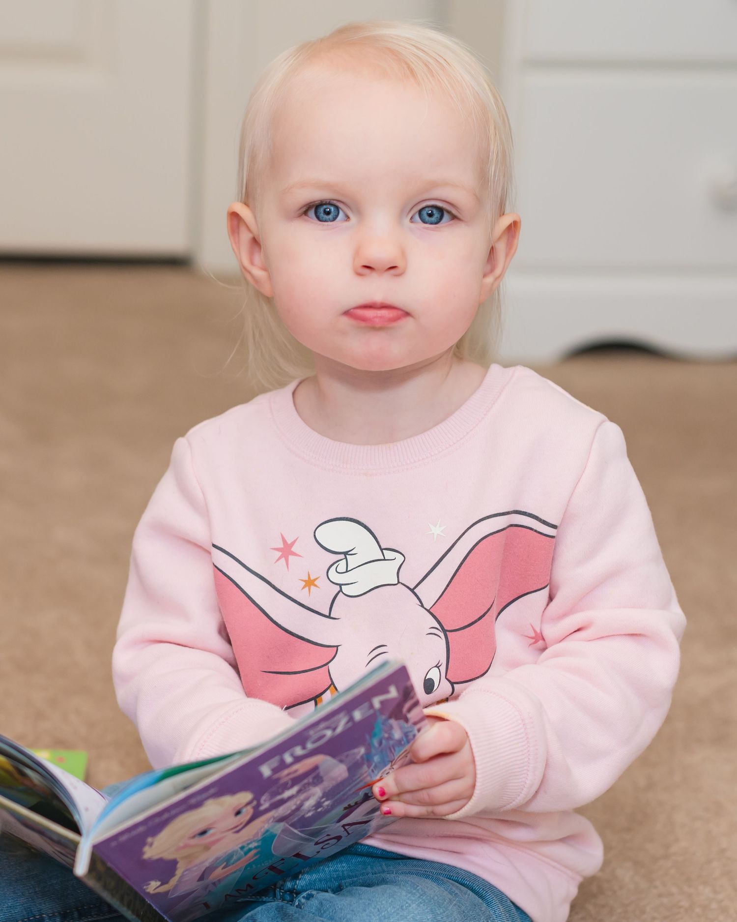 Child in pink sweatshirt with cartoon print holding purple book.