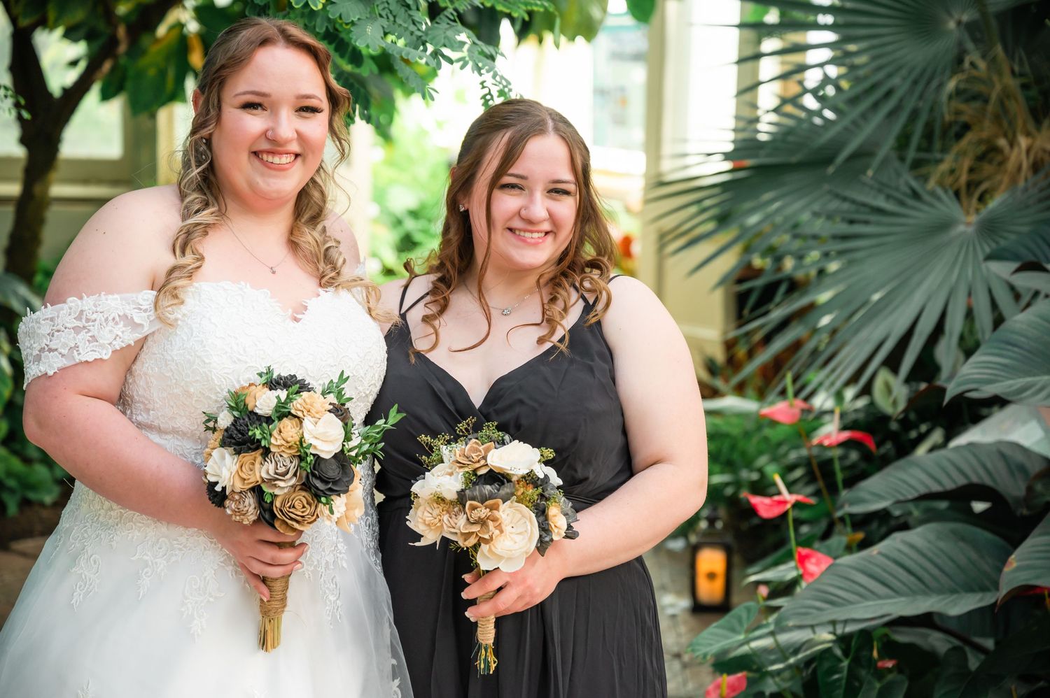 Duo poses with matching floral bouquets in front of tropical garden foliage.