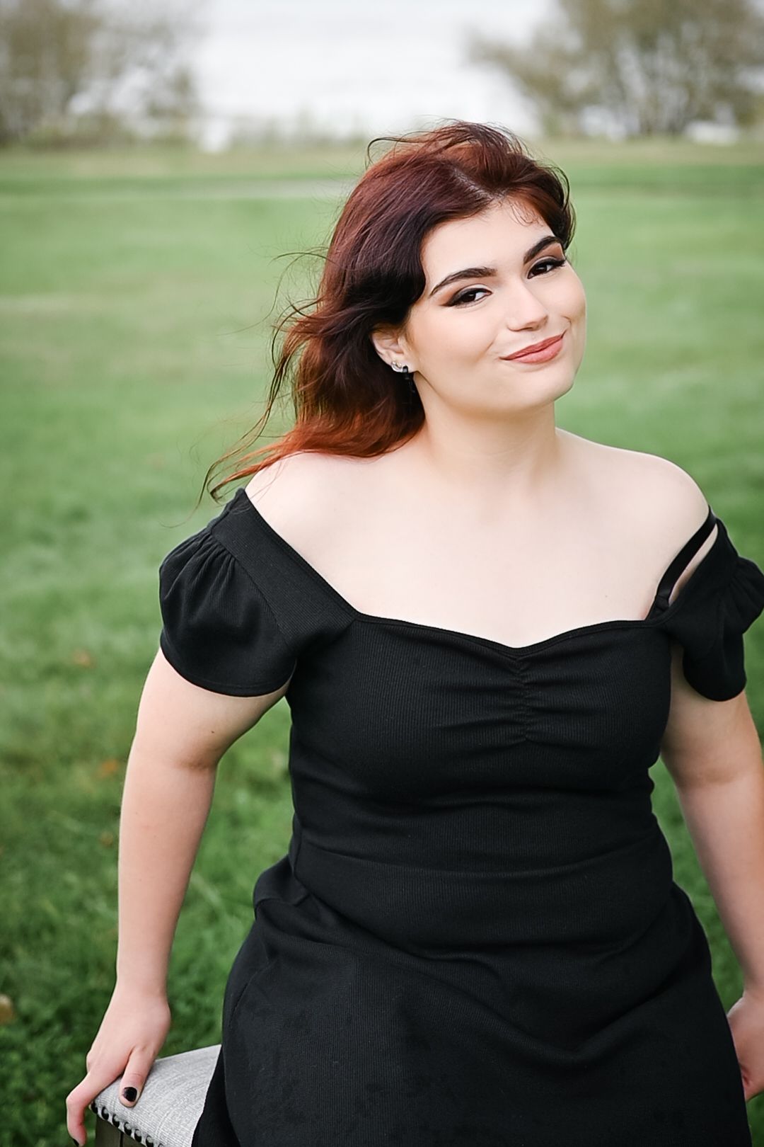 Elegant portrait in black dress with puff sleeves against natural green background.