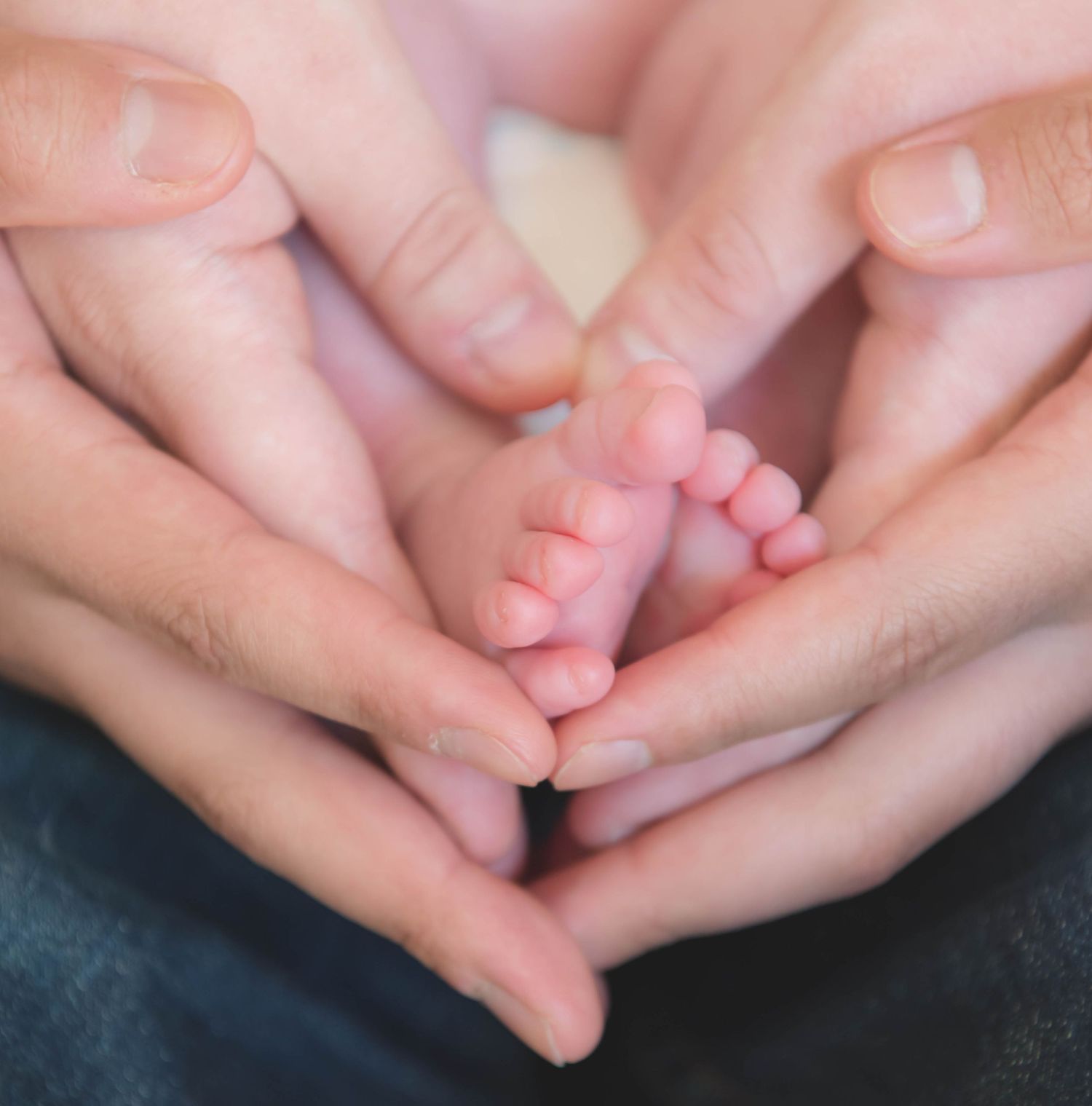 Hands gently holding and massaging tiny baby feet in a sequence of tender poses against a dark background.