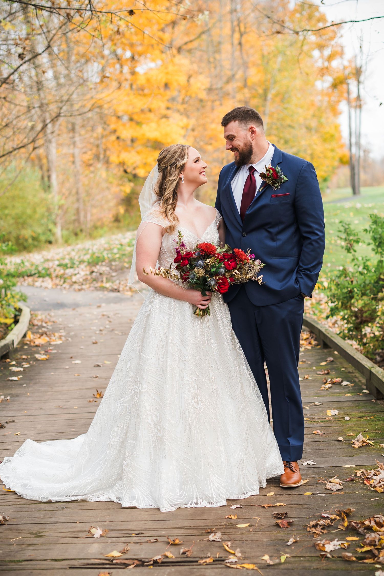 A couple shares a romantic moment on a wooden boardwalk surrounded by autumn foliage.