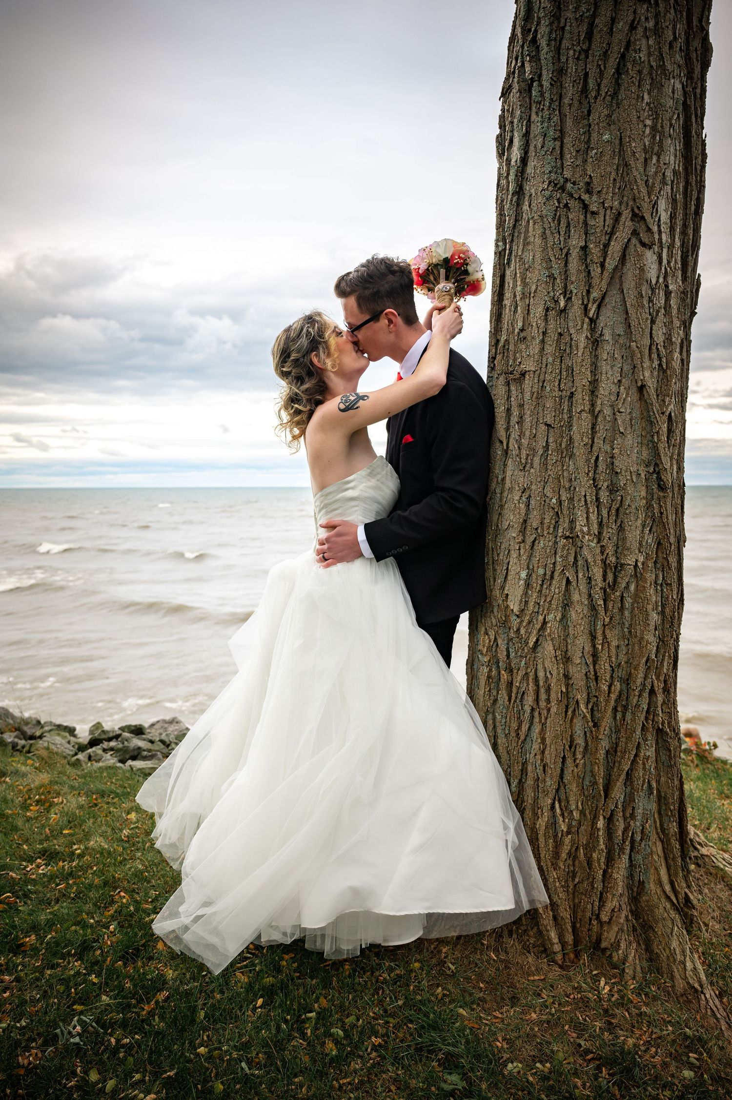 Romantic wedding portrait by a large tree trunk overlooking a dramatic ocean view.