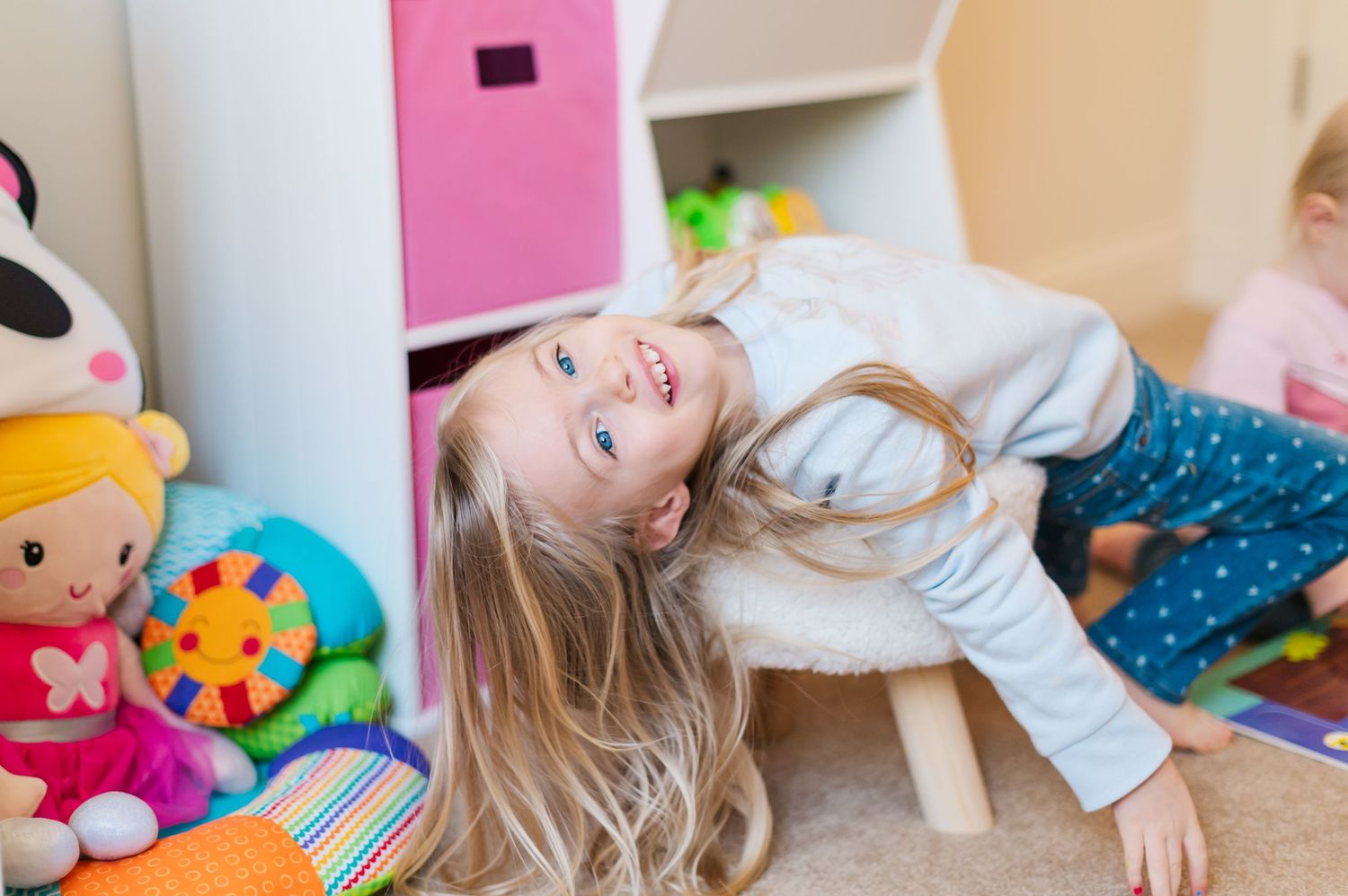 Child lying on floor laughing near pink storage boxes and colorful toys.