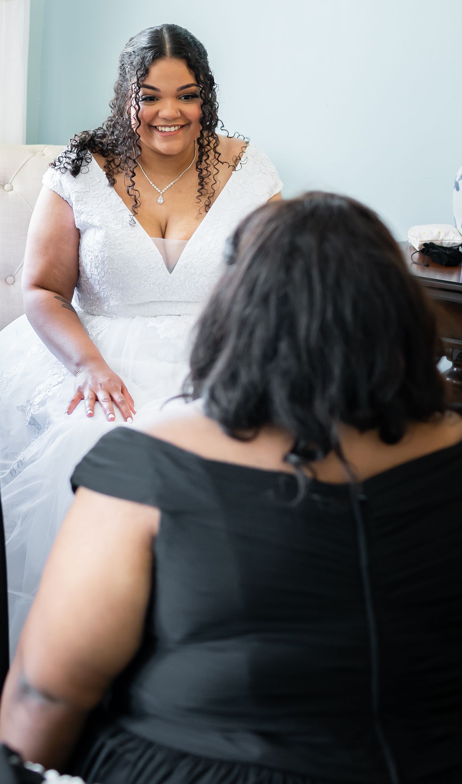 A person in a white wedding dress smiles while seated during pre-wedding preparations.