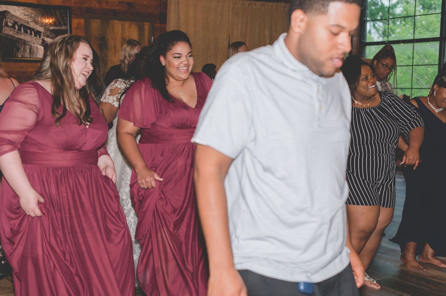 Wedding party in burgundy dresses dancing at reception celebration.