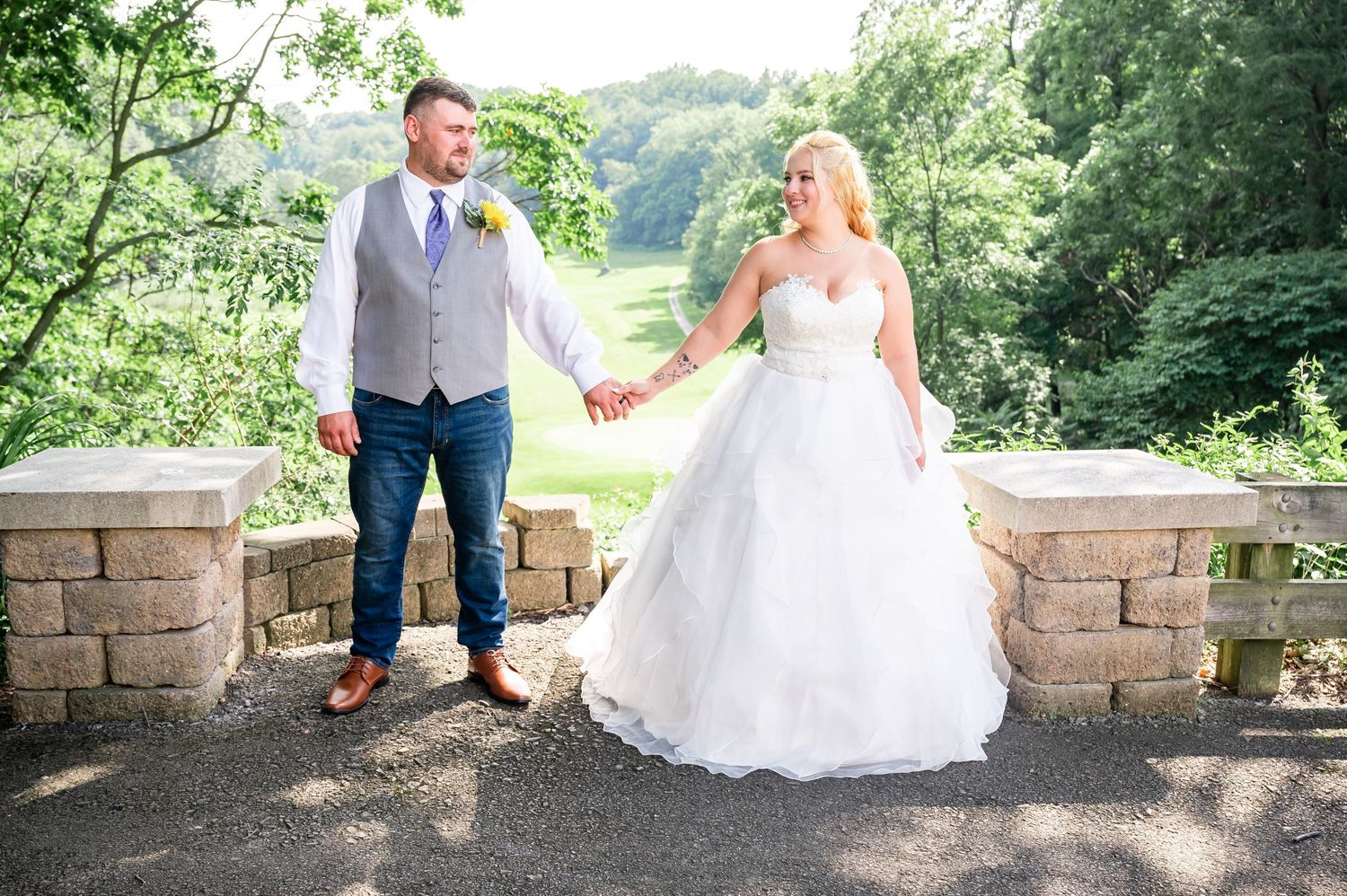 Wedding couple holding hands while standing on stone wall overlook.