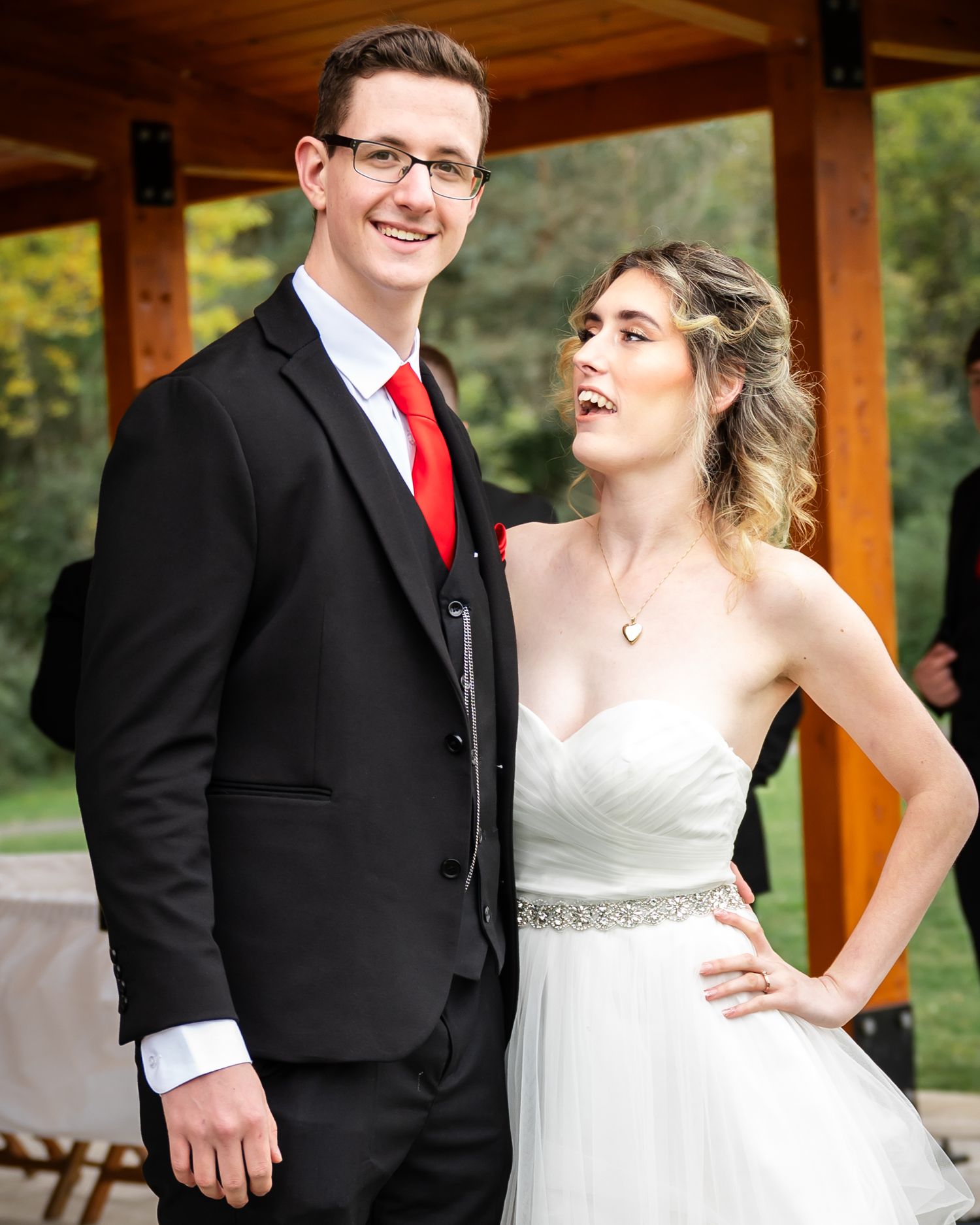 A couple shares a candid moment under a wooden pavilion at their wedding.