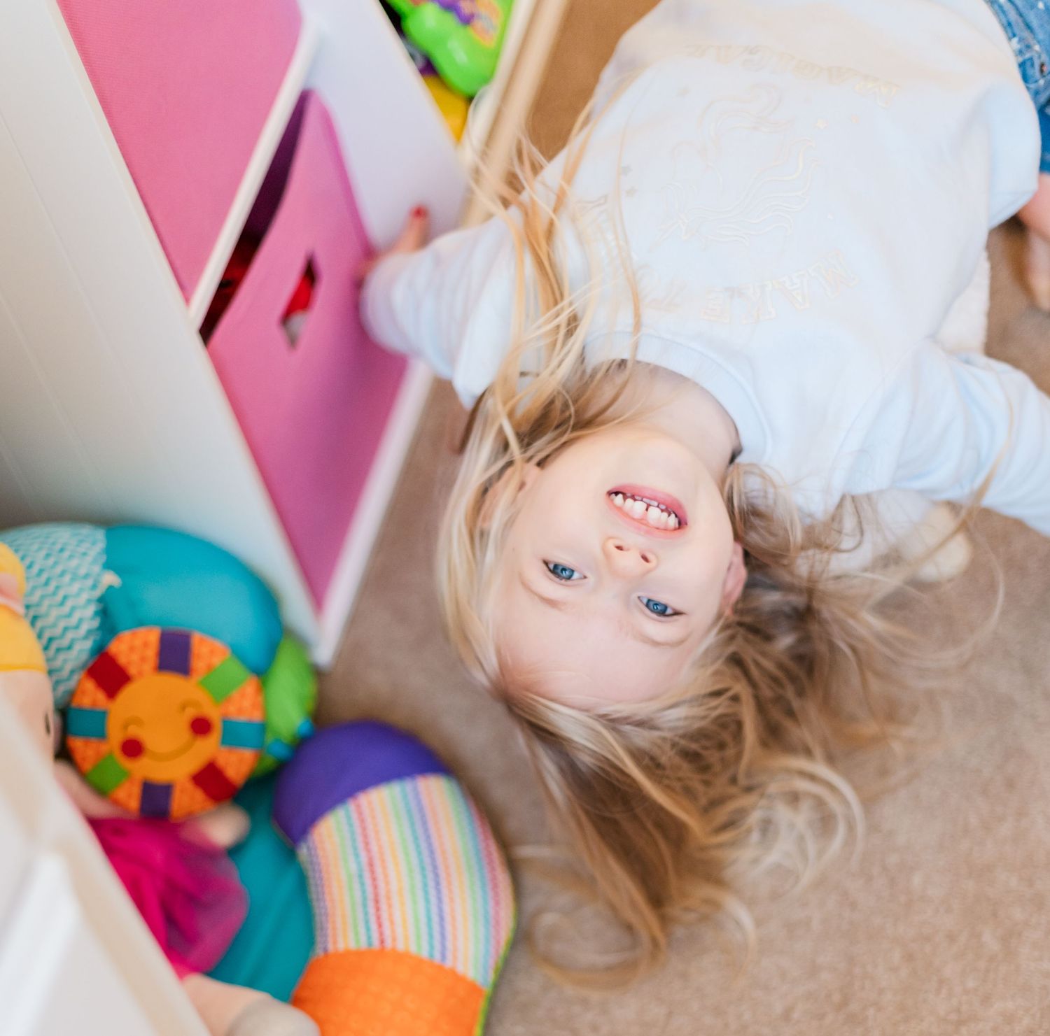 Child lying down and playing among colorful toys and stuffed animals.