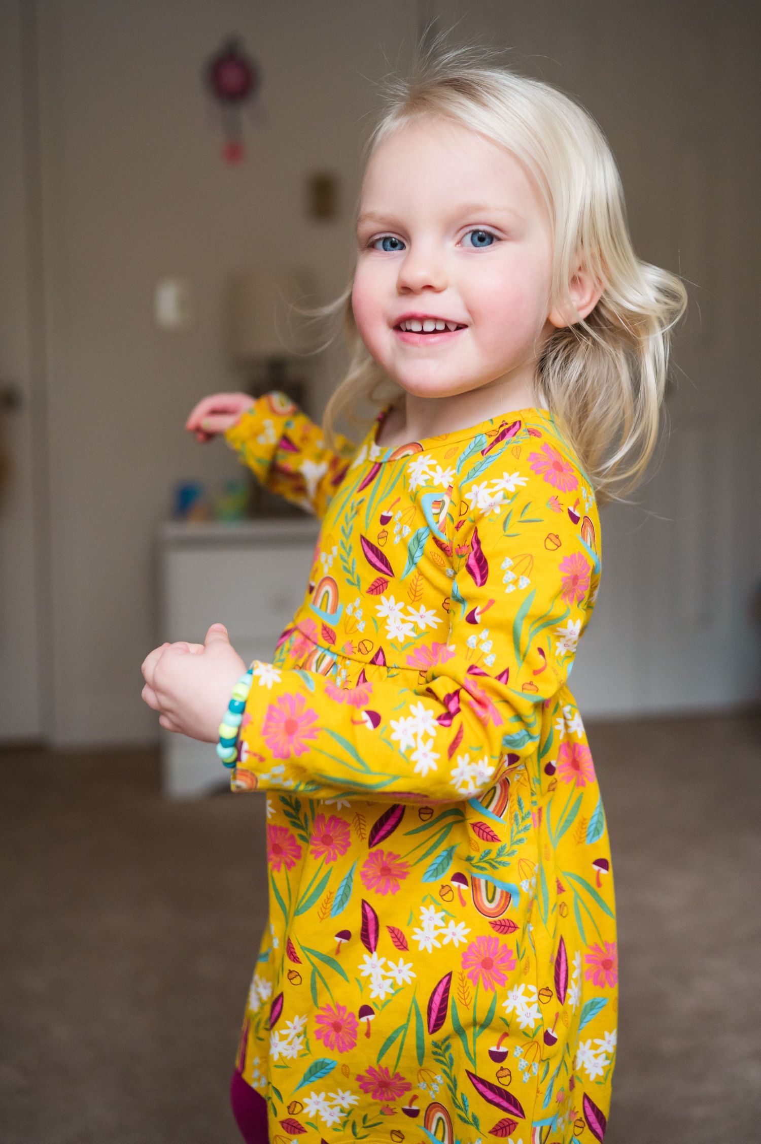 A child in a vibrant yellow floral dress playing indoors with a toy.