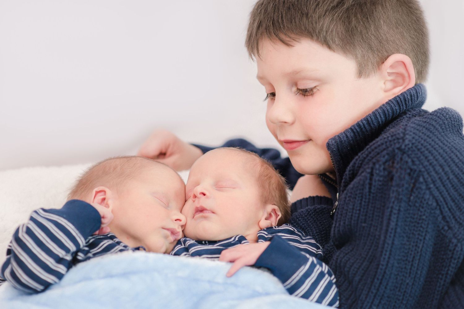A sleeping child in a navy blue sweater rests peacefully on white bedding.