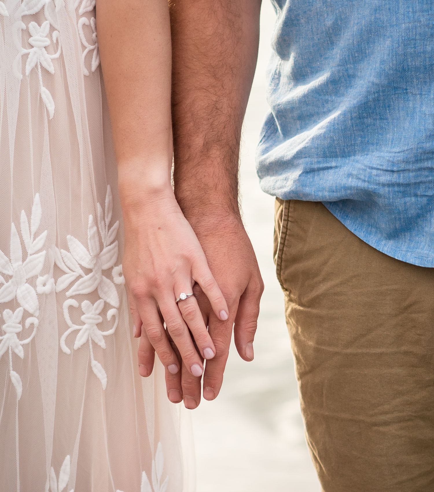 A person wearing a blue shirt and khaki pants holds their hands together against a floral backdrop.