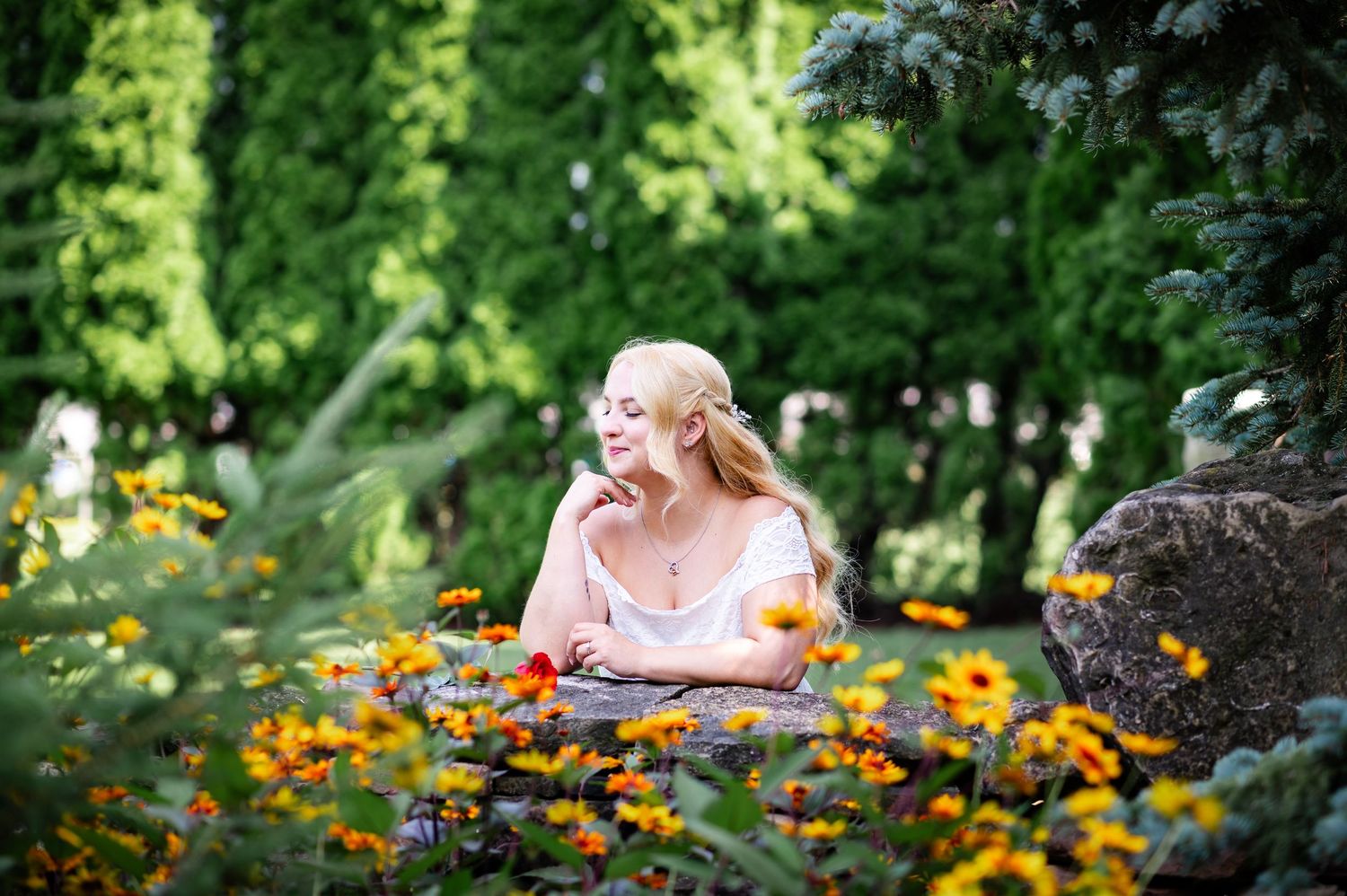 A woman in a pink dress sits thoughtfully in a vibrant garden filled with orange and yellow flowers.