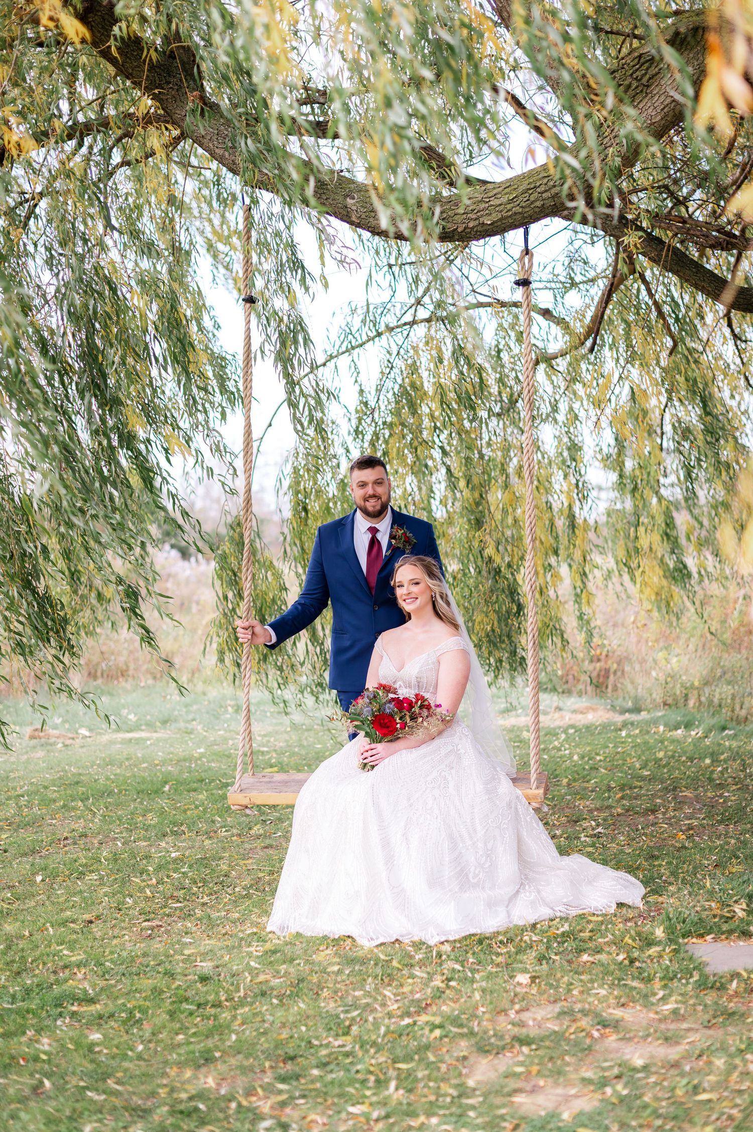 Romantic portrait under willow tree with couple on wooden swing.