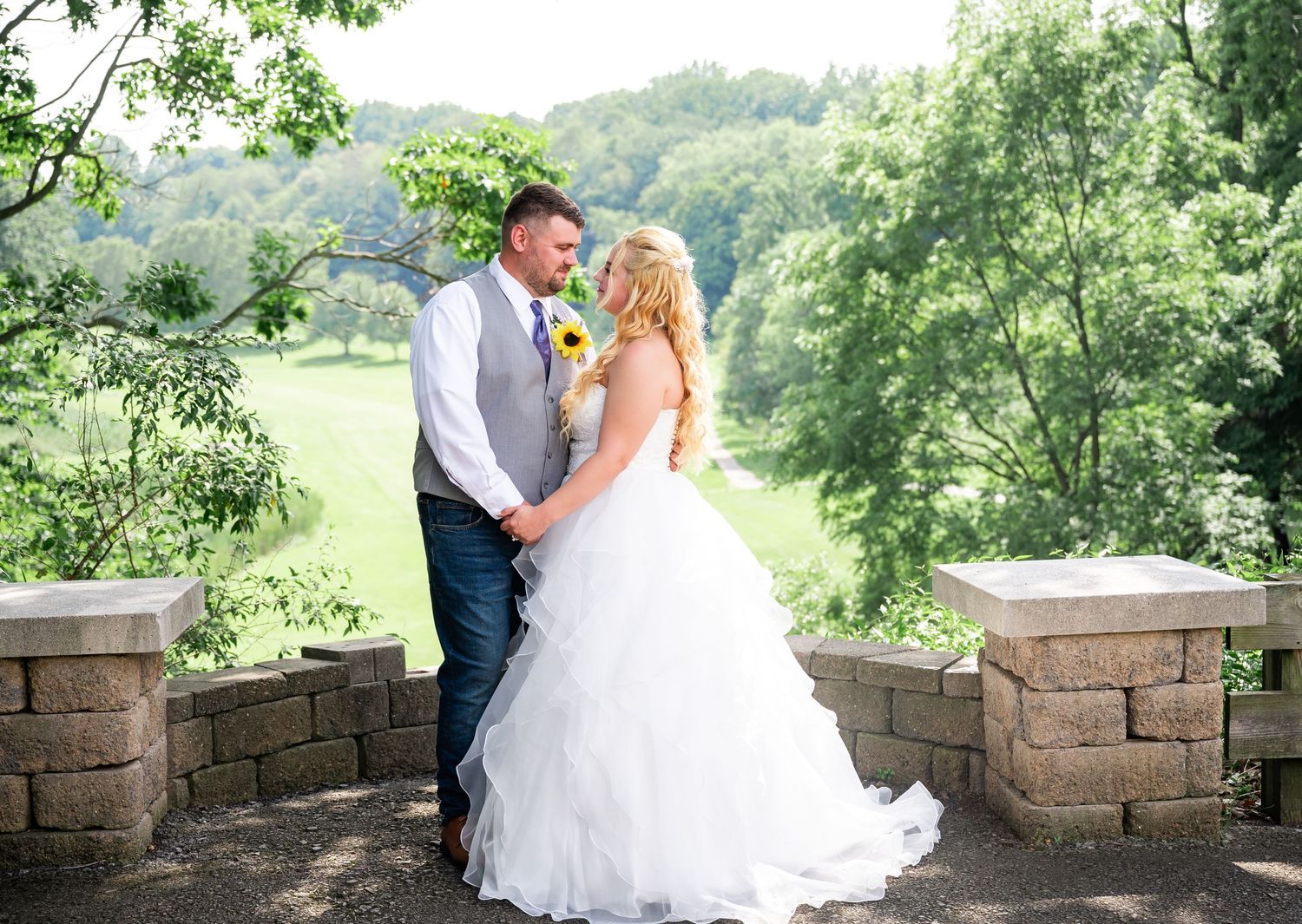 Newlyweds share romantic pose on stone terrace surrounded by lush greenery.