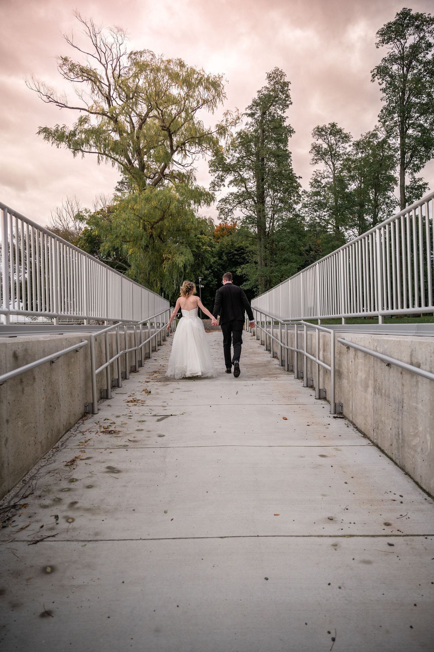 Couple walking away on white railed bridge pathway under cloudy sky.