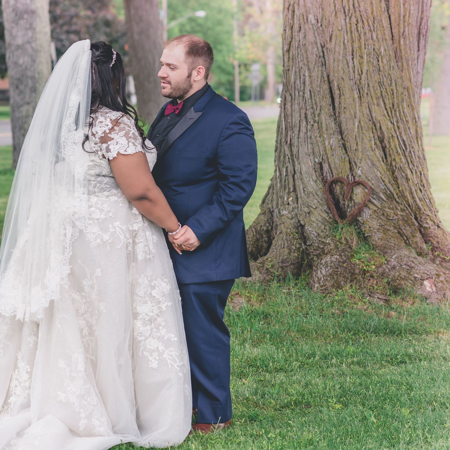 A romantic wedding portrait captured outdoors near a large tree trunk.