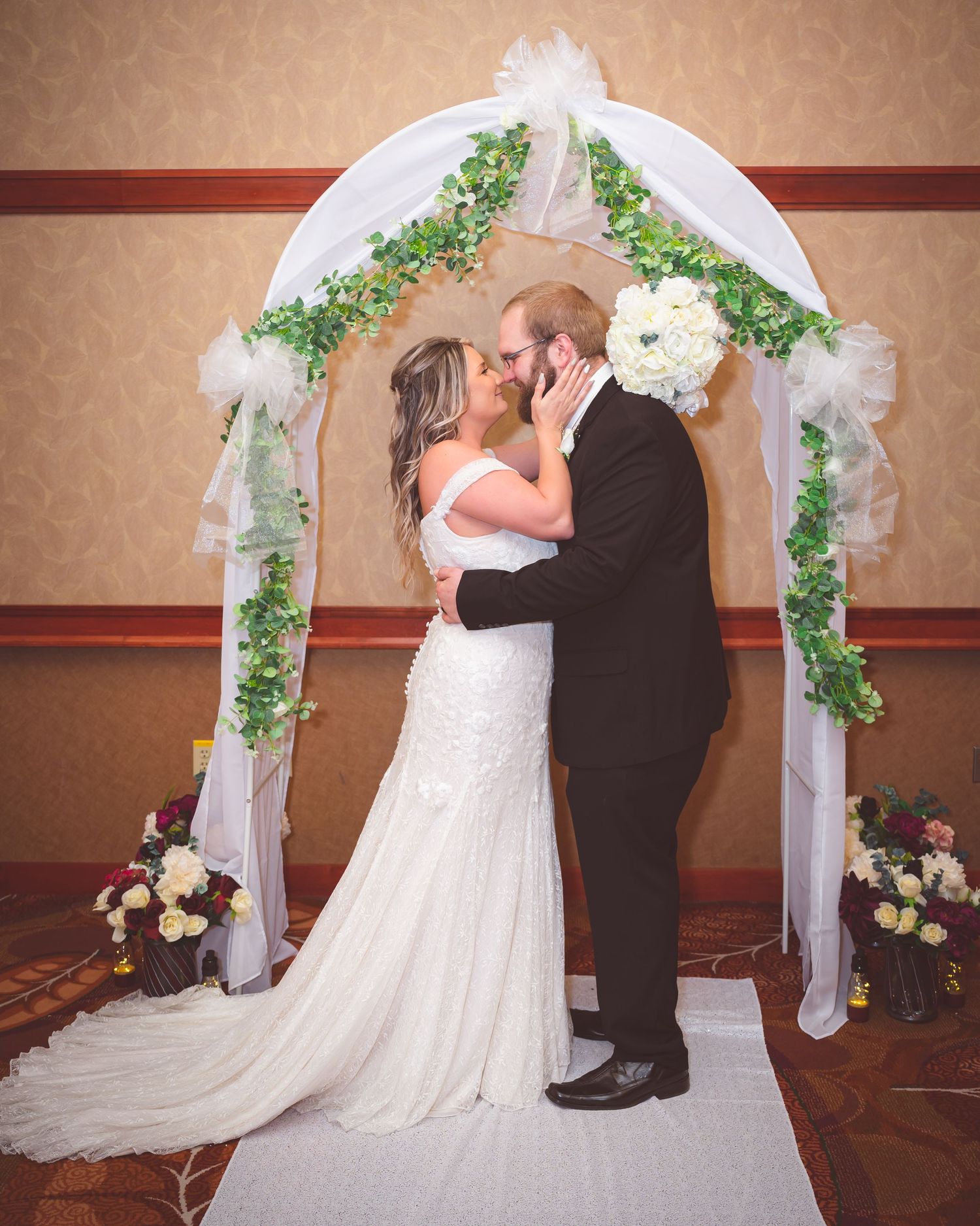 Newlyweds share romantic moment under floral wedding arch during ceremony.