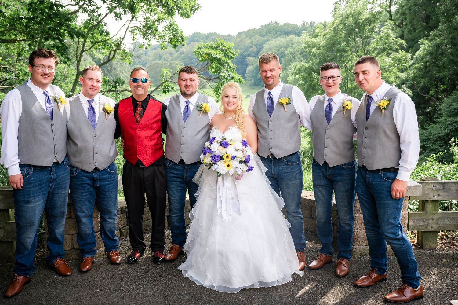 Wedding party in gray vests and jeans poses together on stone terrace.