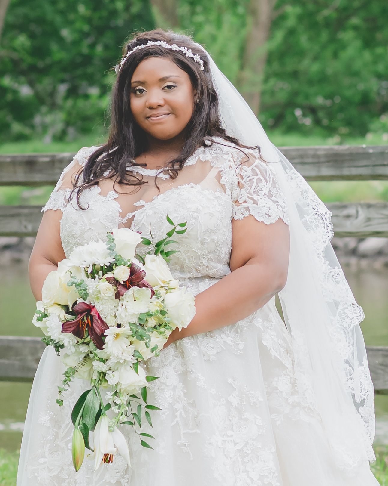 A radiant bride in lace holds a stunning bouquet of white and burgundy flowers.