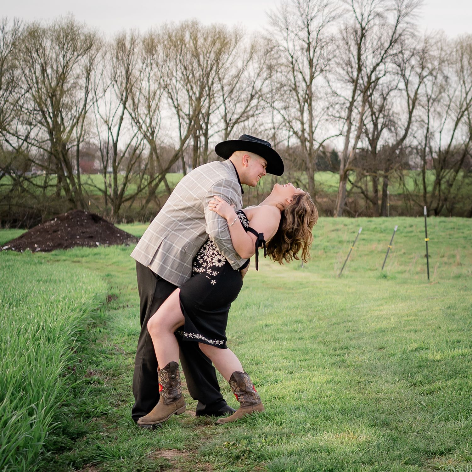A couple in country attire shares a romantic dip pose in a green spring field.