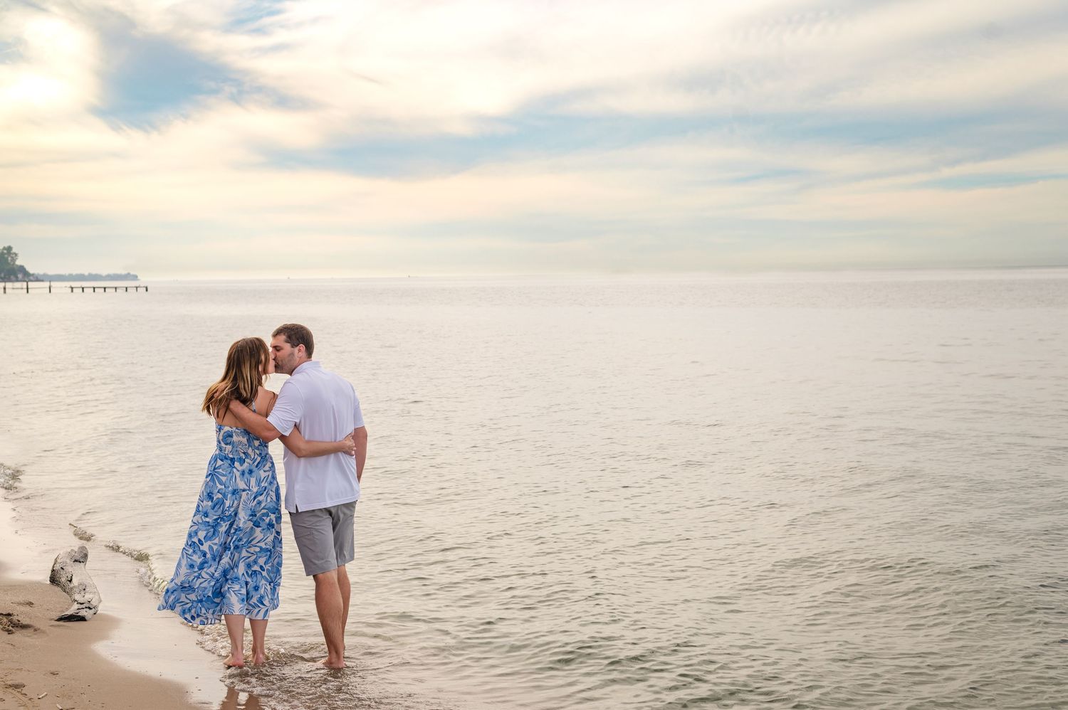 Couple in coordinated blue and white outfits walking together along a serene beach at sunset.