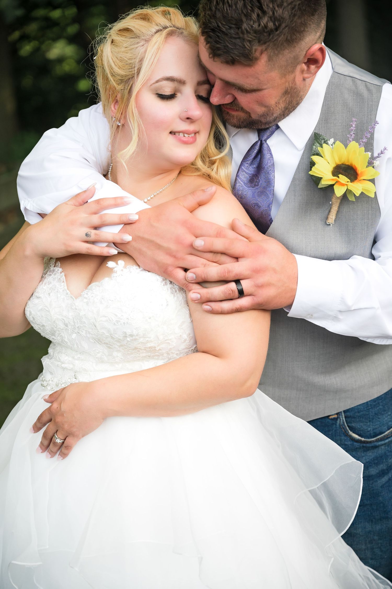 Romantic wedding moment with couple embracing outdoors, showcasing rings and sunflower boutonniere.