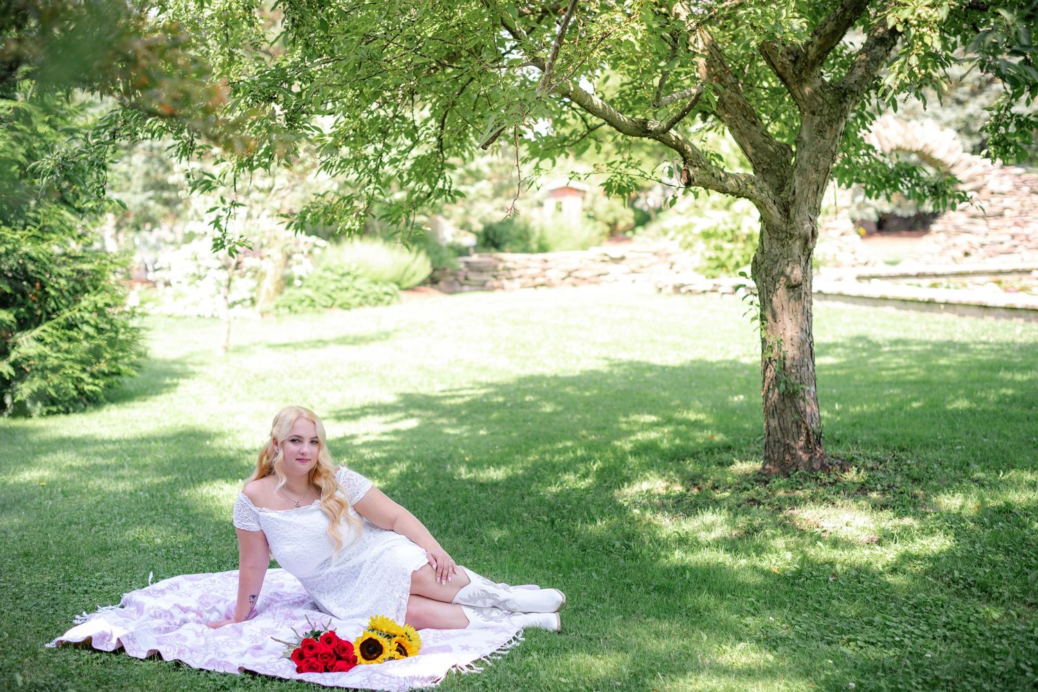 A serene summer garden scene with flowers and a white blanket under a tree.