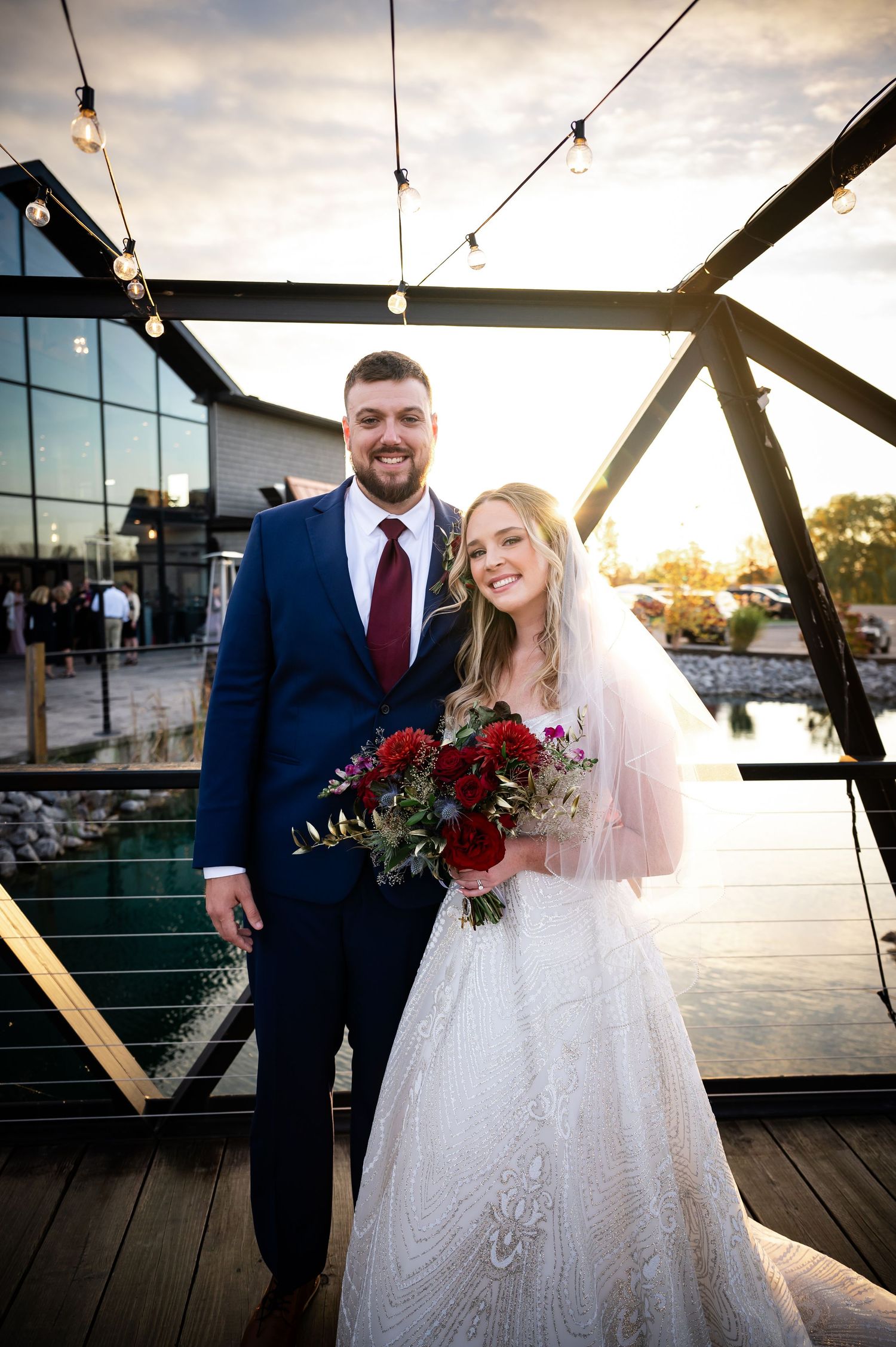 A couple poses for wedding photos at sunset on a wooden deck with scenic waterfront views behind them.