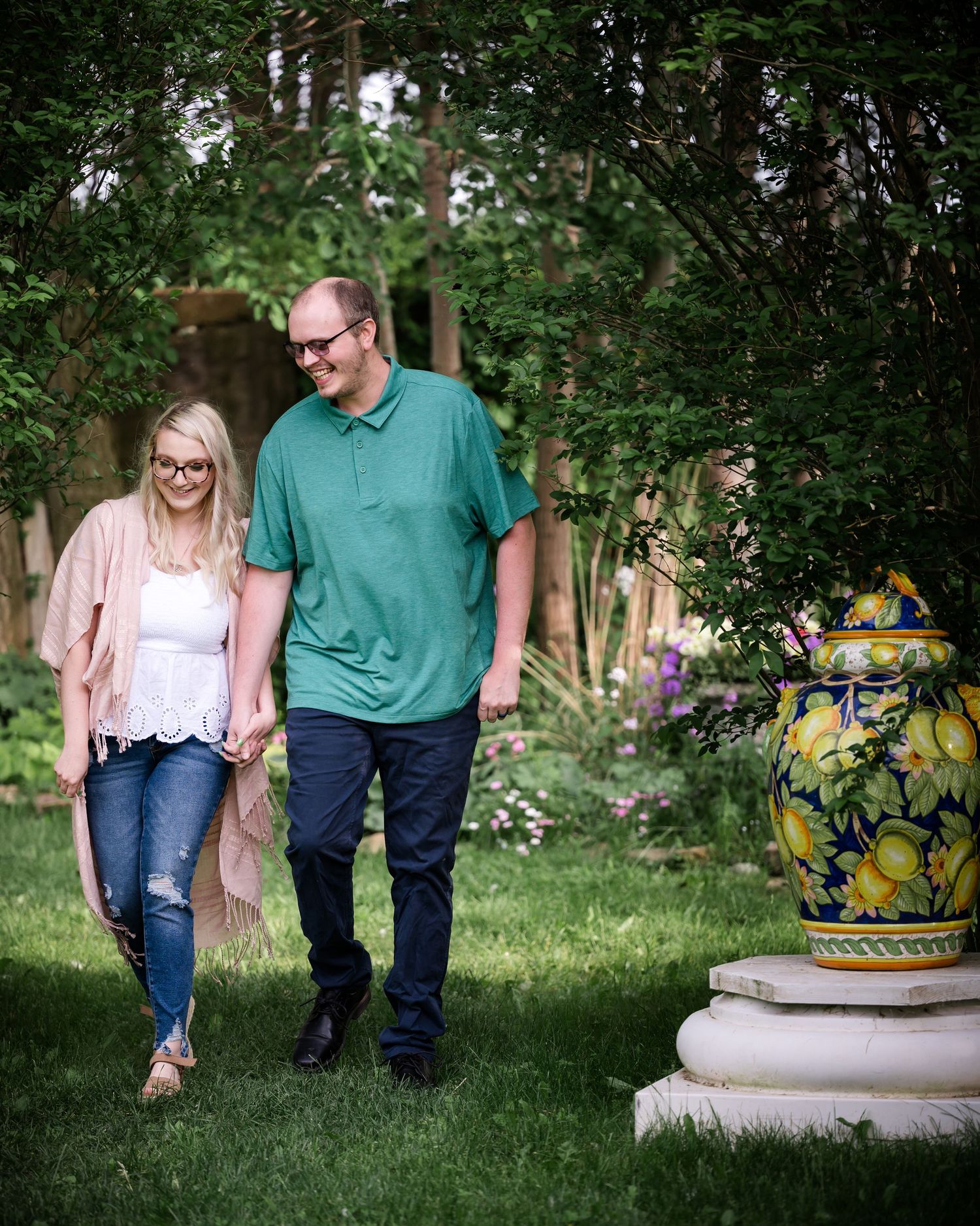 Casual couple walking through garden with decorative urn and blooming flowers.
