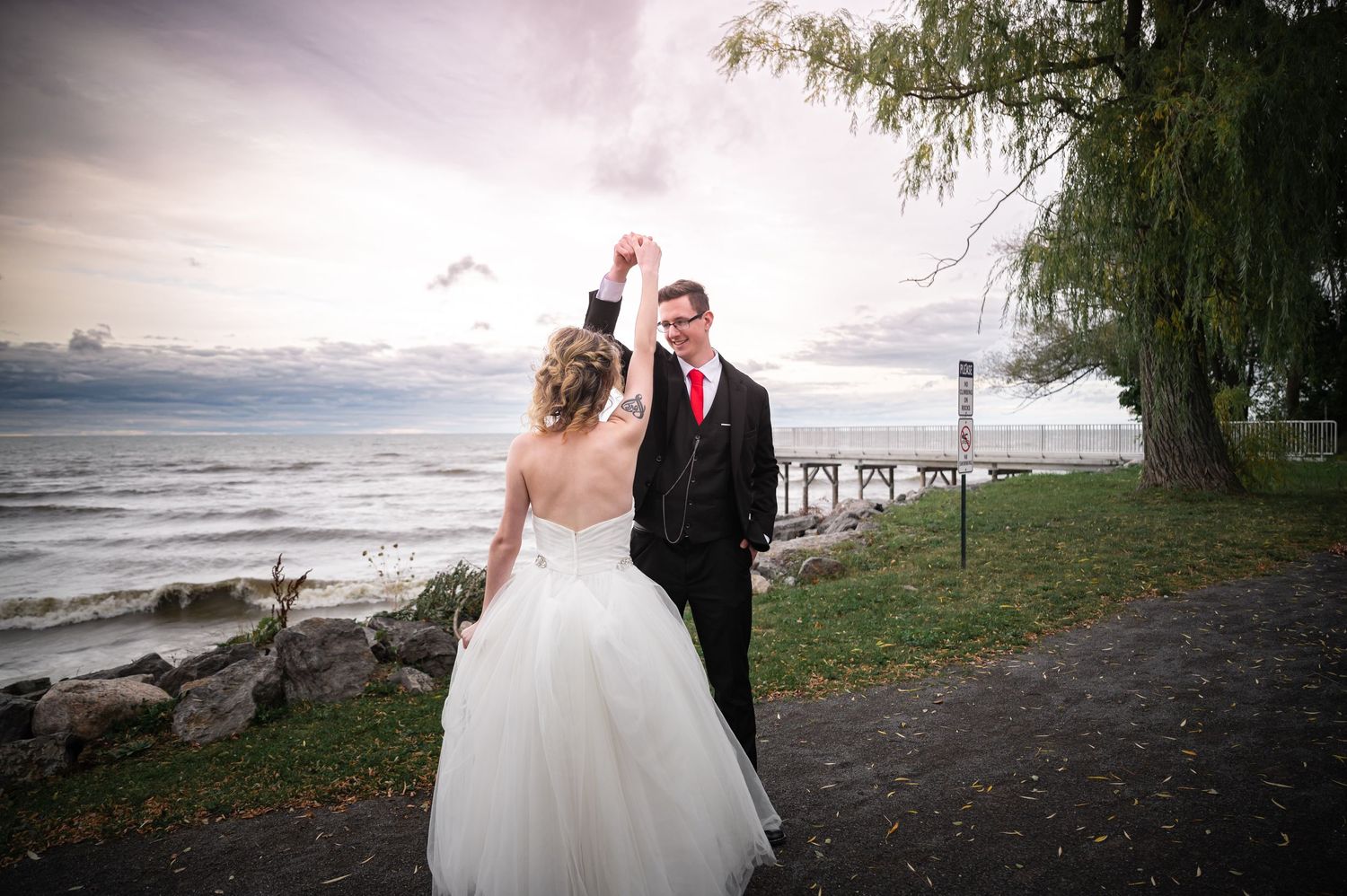 A couple stands on a path overlooking the ocean with a dramatic cloudy sky behind them.