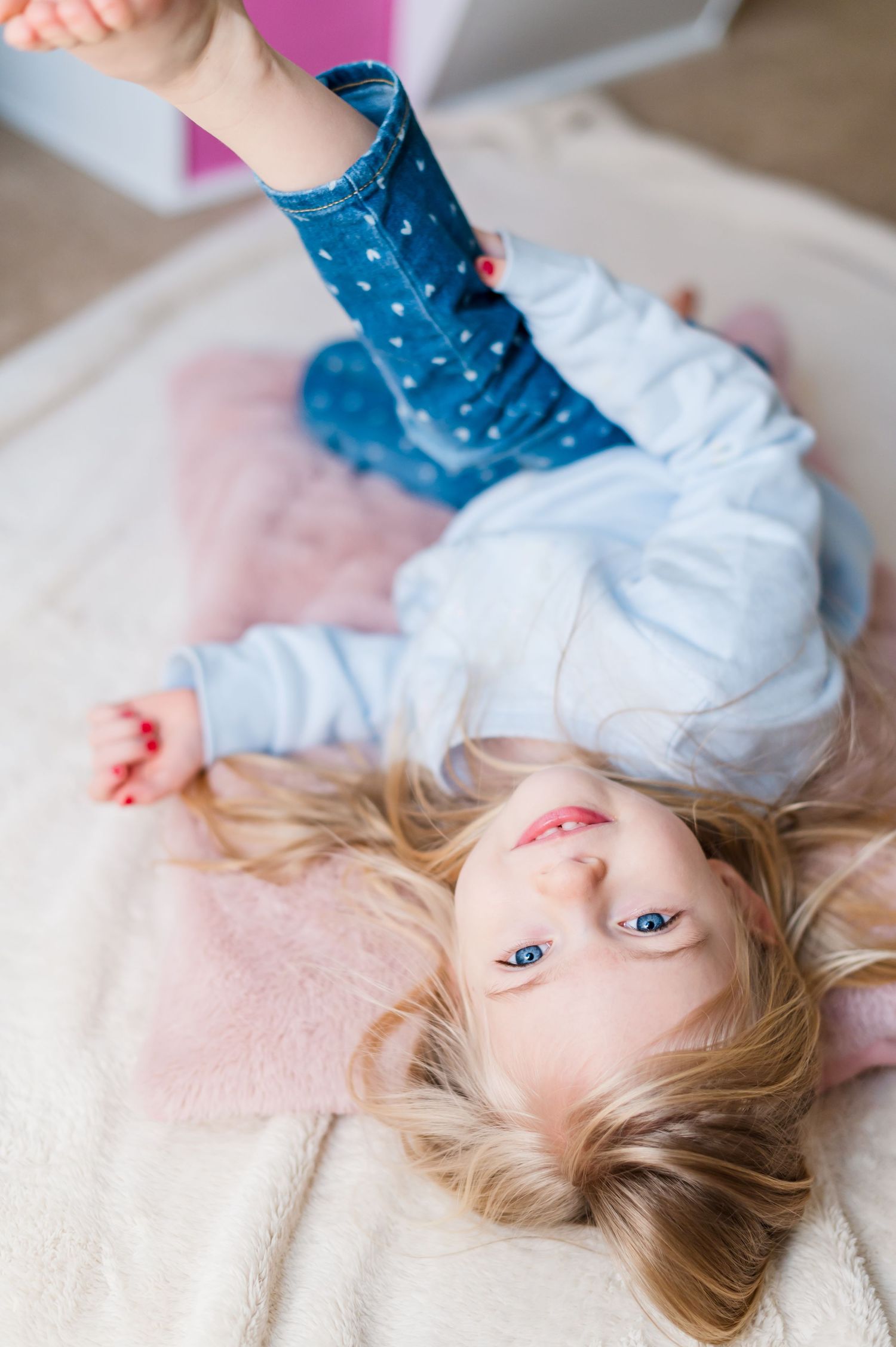 Child lying on pink blanket wearing polka dot pants and light sweater.