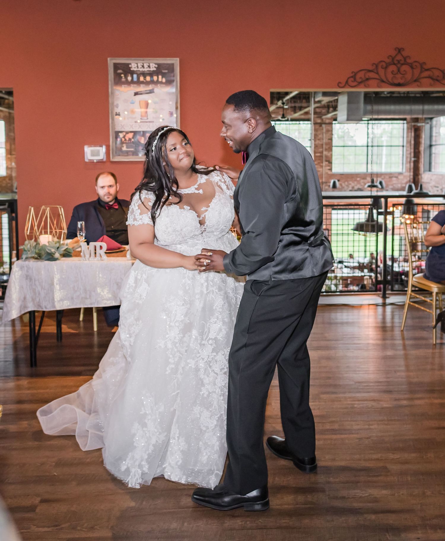 A tender moment shared during a wedding dance in a venue with coral walls and wooden floors.