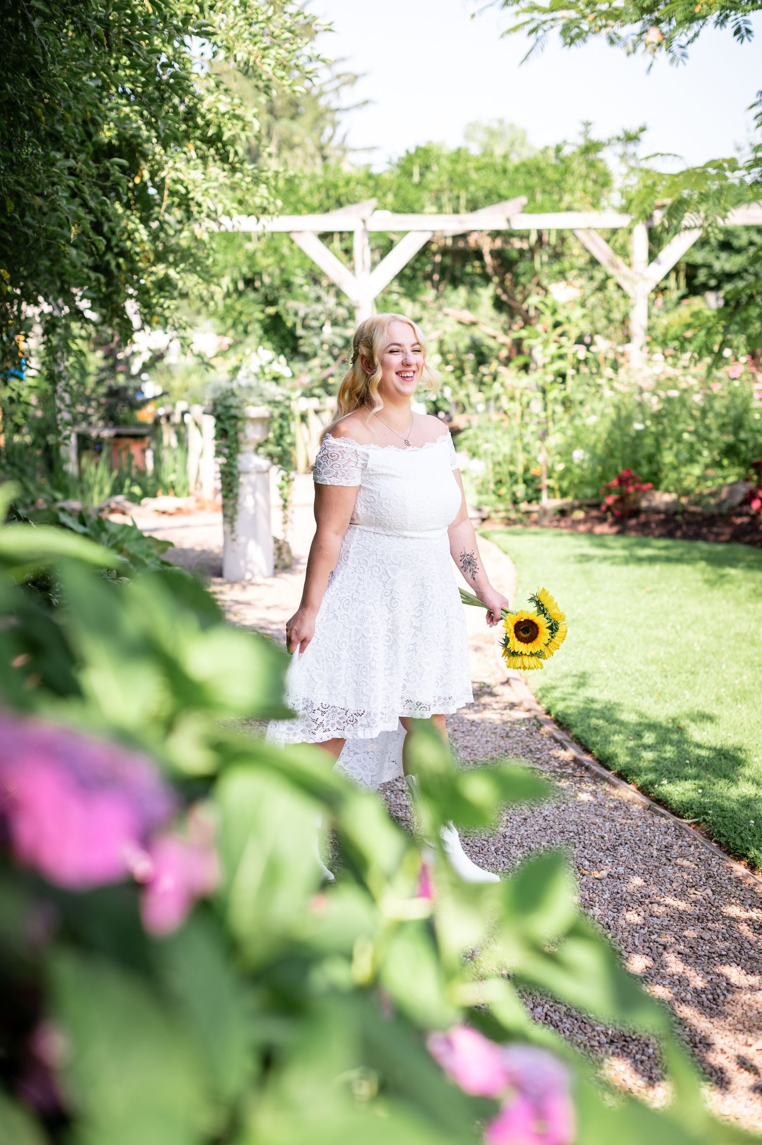 Romantic garden photoshoot with white dress and sunflower among colorful blooms.