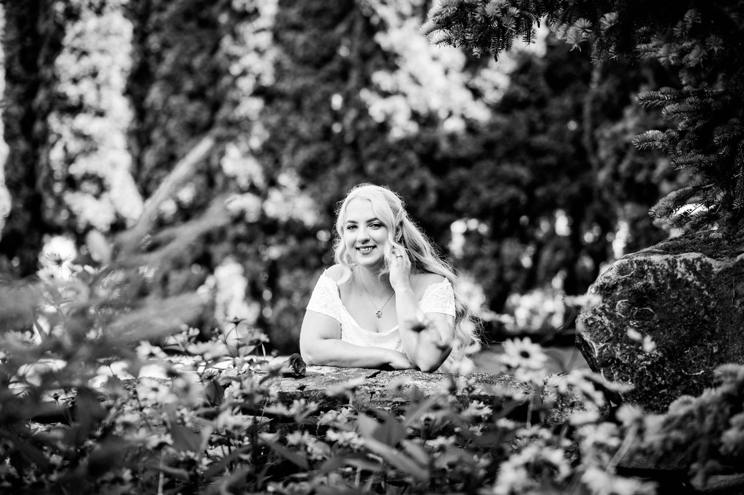 Black and white portrait of person resting on stone wall in garden setting.