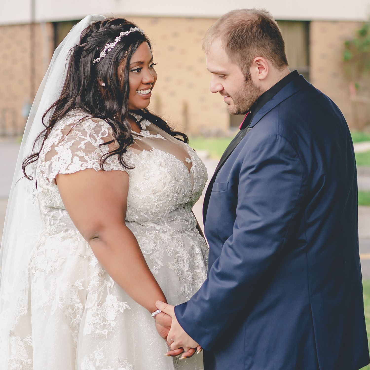 Bride and groom share an intimate moment outdoors on their wedding day, with bride in lace dress and groom in navy suit.
