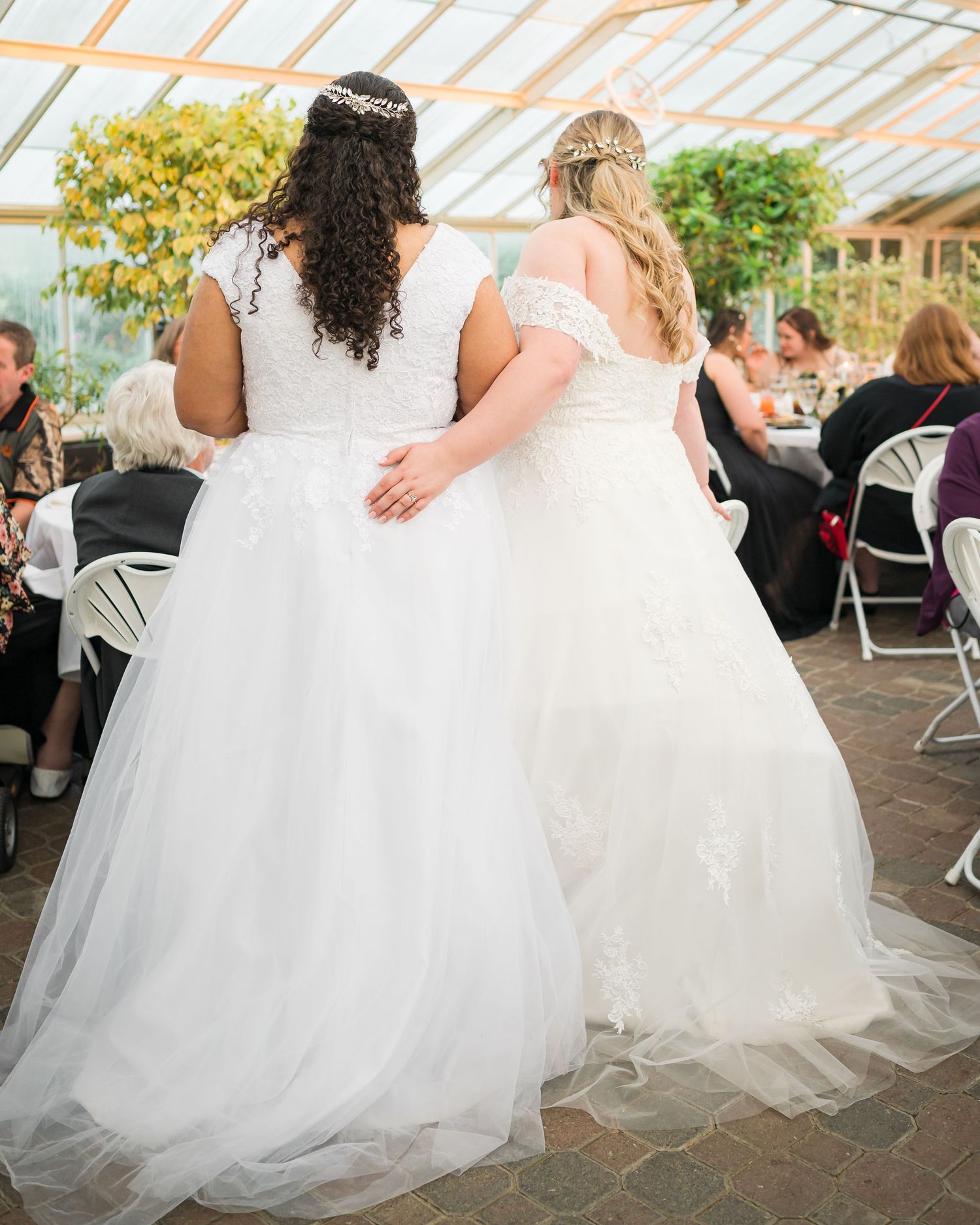 Two brides in white wedding gowns stand together during their reception.