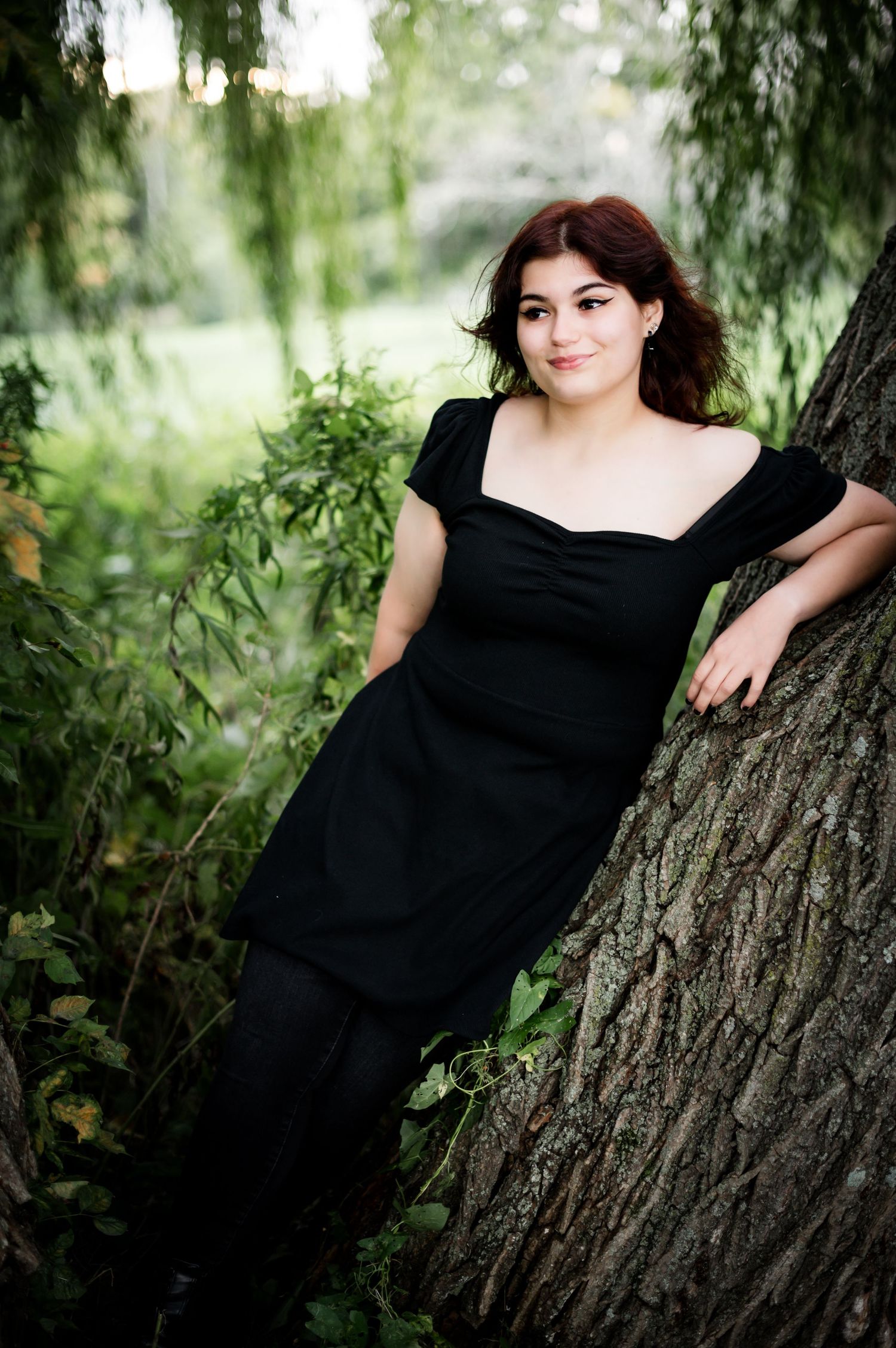 Romantic portrait leaning against a large tree trunk surrounded by lush greenery.