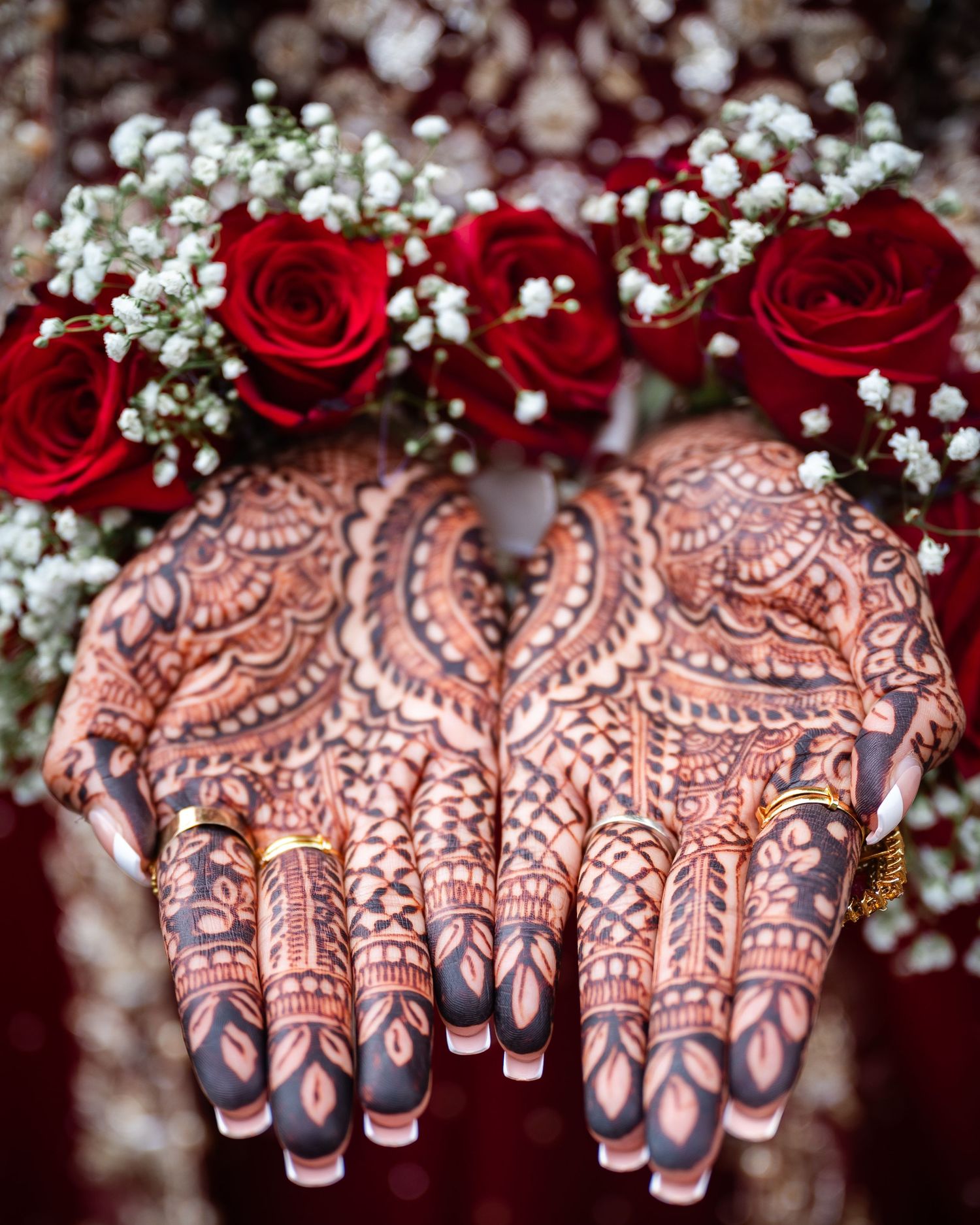 Intricate henna designs on hands with red roses and baby's breath flowers in the background.