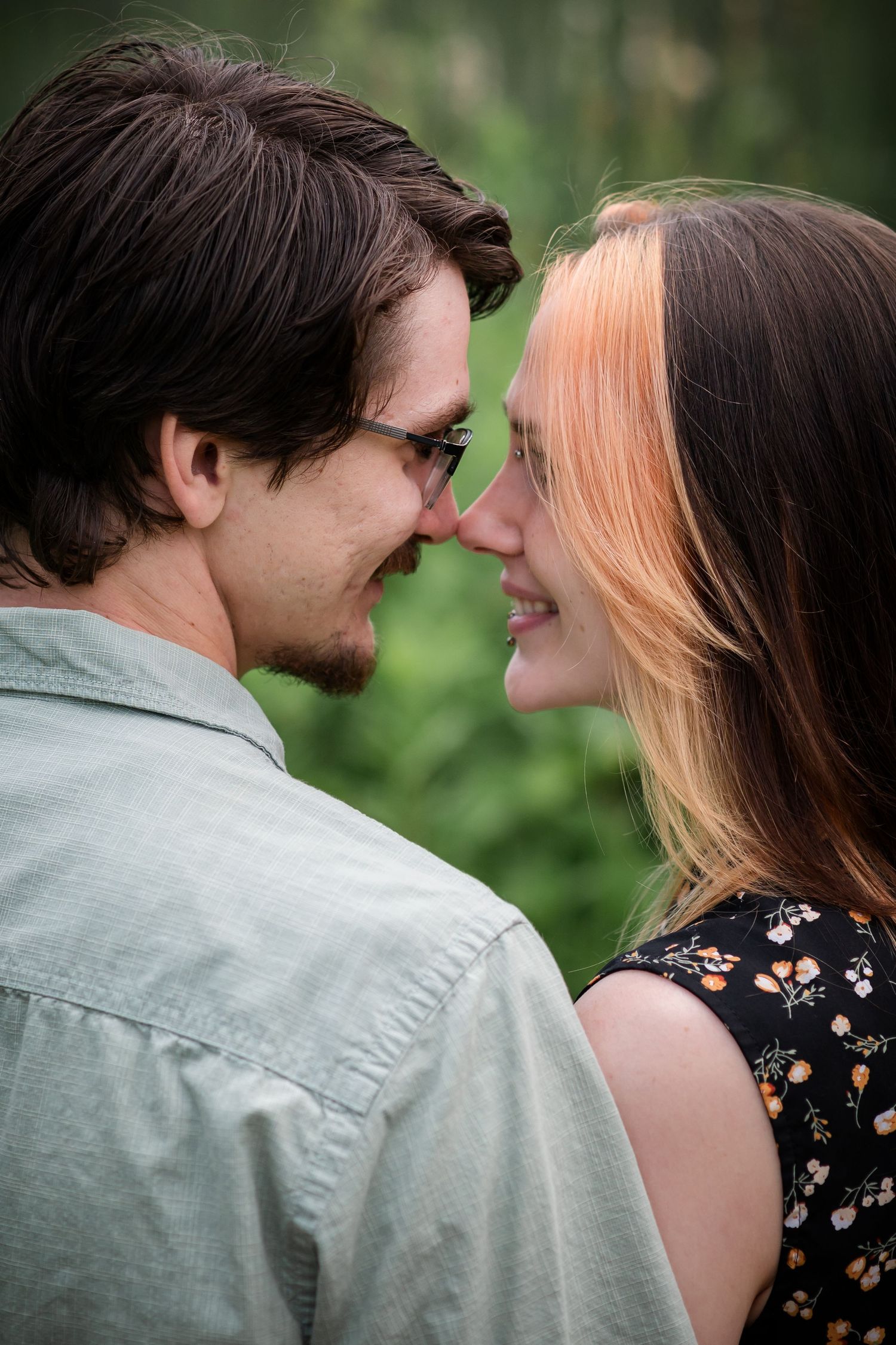 Intimate close-up moment between couple against blurred green background.