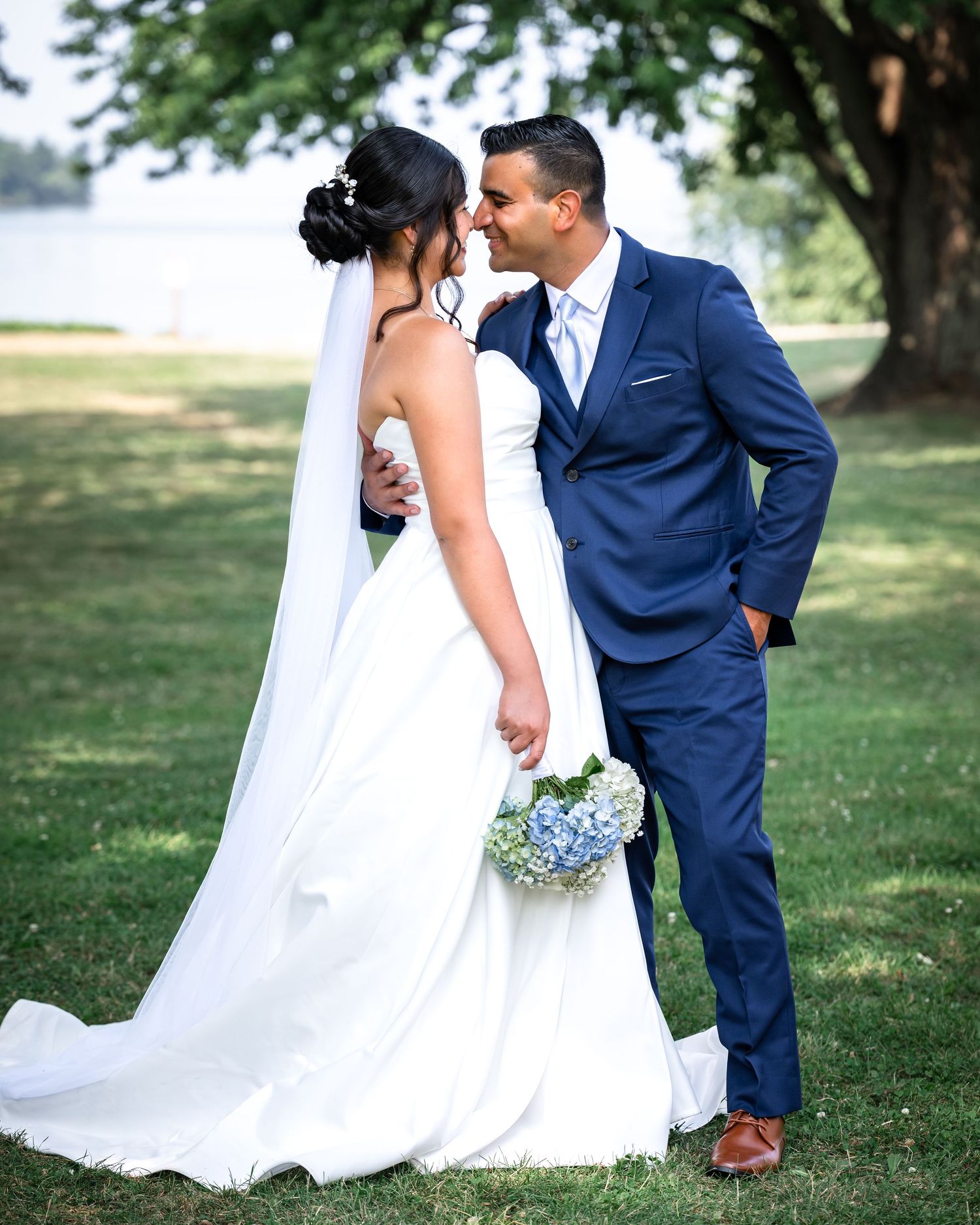 A bride and groom share an intimate moment in a garden setting while wearing navy blue suit and white wedding dress.