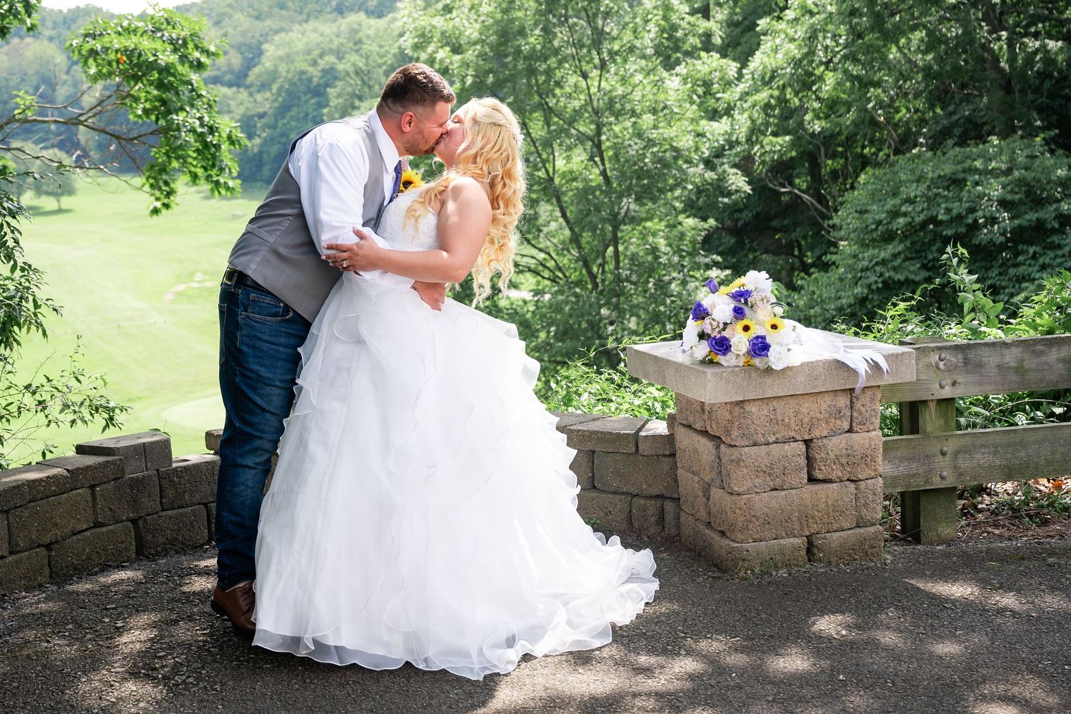 Wedding couple sharing kiss on scenic overlook with stone wall.