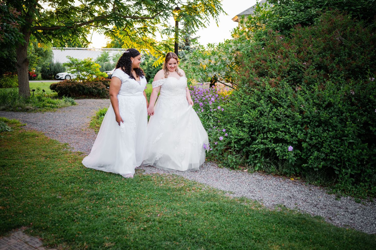 Two wedding gowns in an outdoor garden setting with a gravel path.
