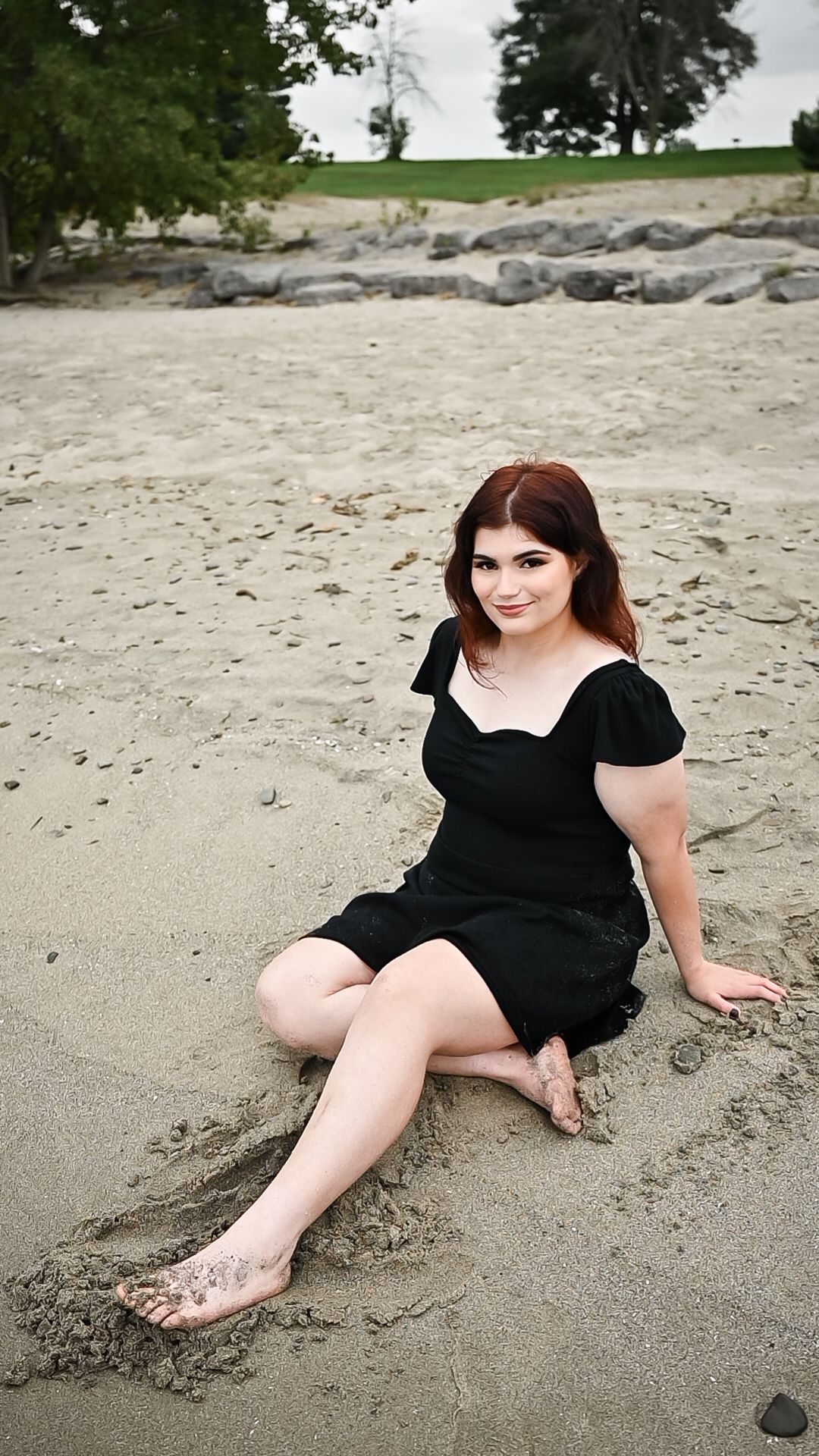 A black dress on sandy beach with rocks and trees in the background.